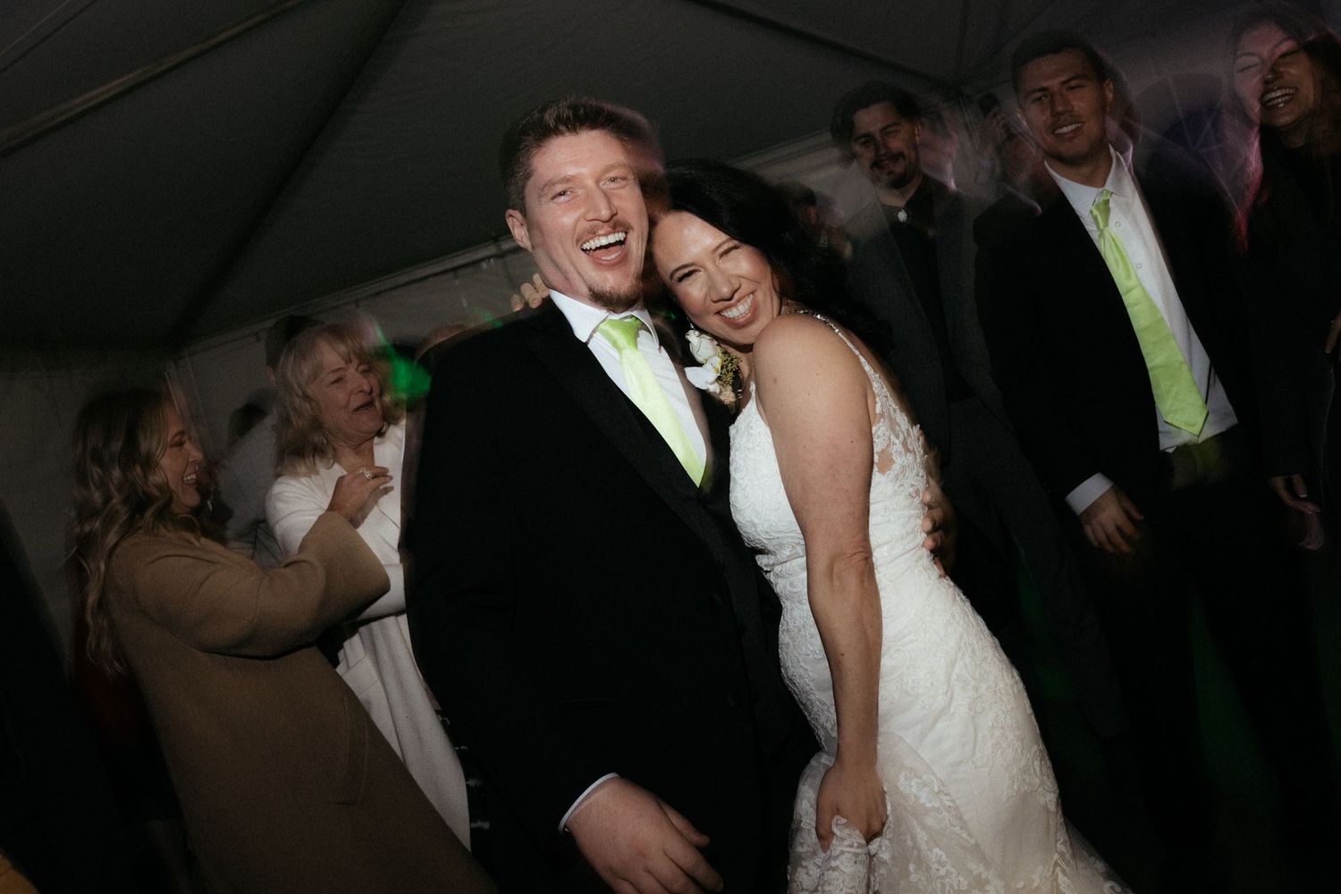 Wedding guests dancing and celebrating together on a dimly lit dance floor at an evening reception.