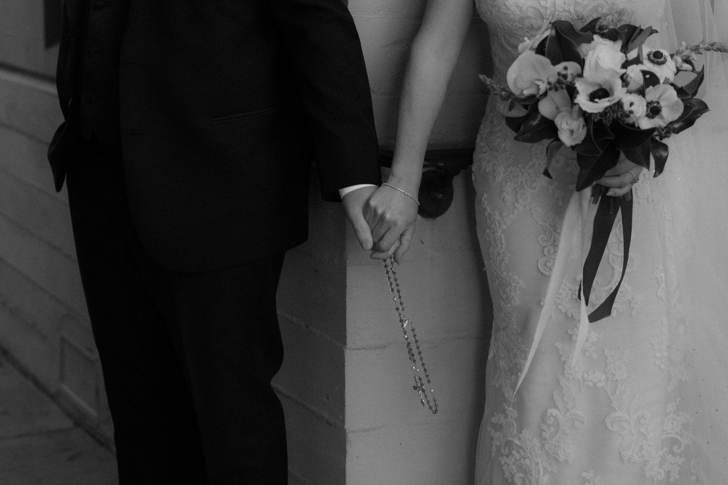 Black and white wedding photo showing couple holding hands with bride holding floral bouquet.