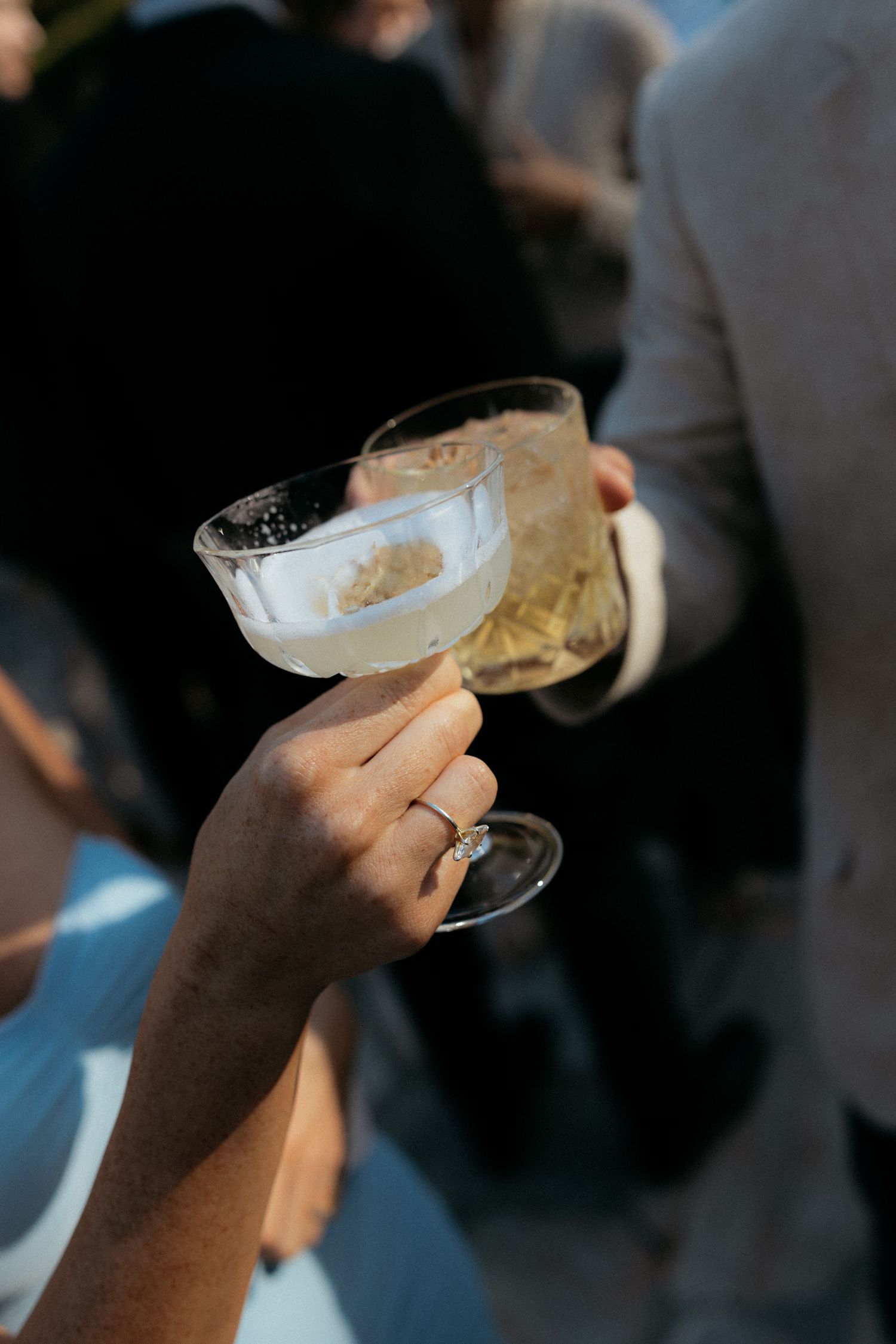 A bride wearing a diamond ring toasts with a coupe glass of champagne at an elegant wedding reception.