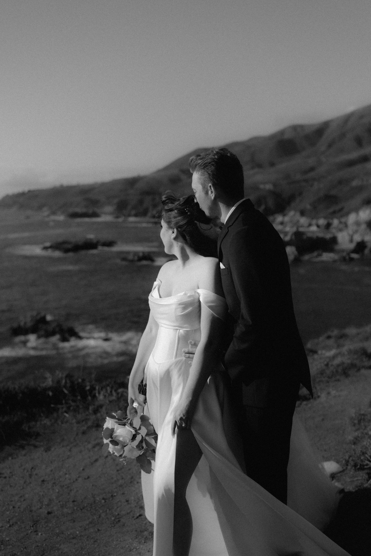 Black and white photo of bride and groom overlooking coastal cliffs on their wedding day.