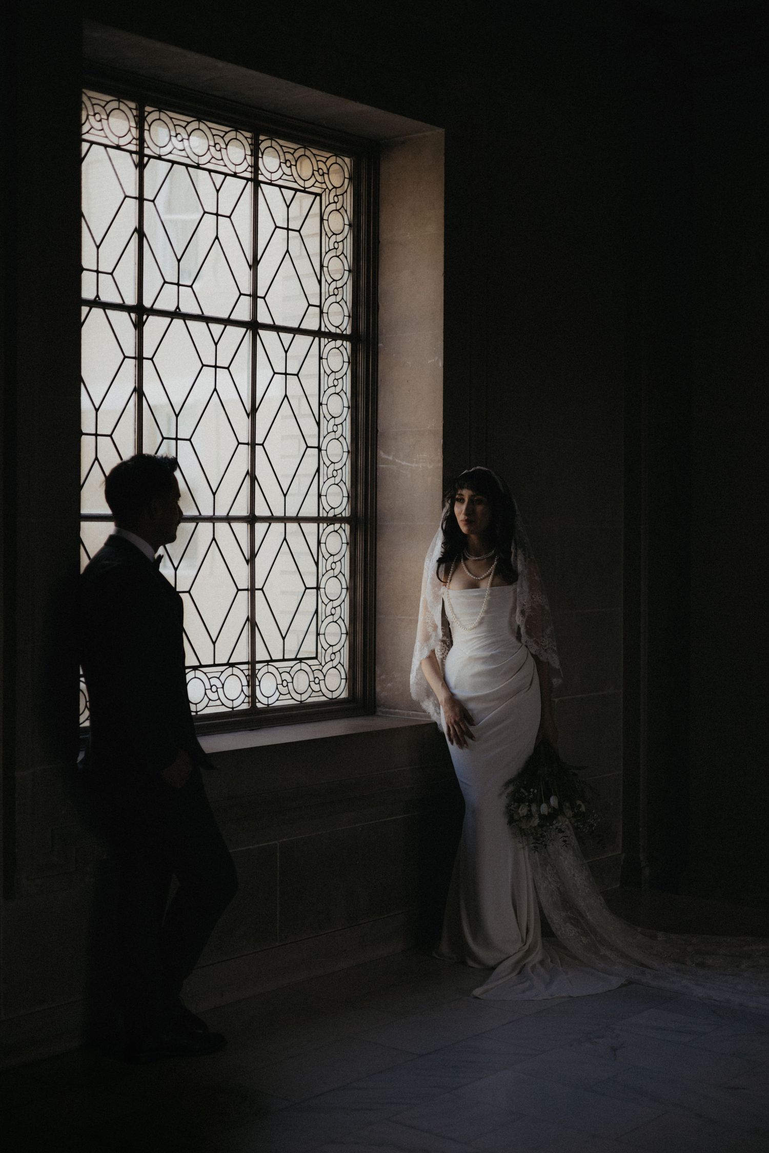 A dramatic silhouette of newlyweds against a geometric window in a historic building.