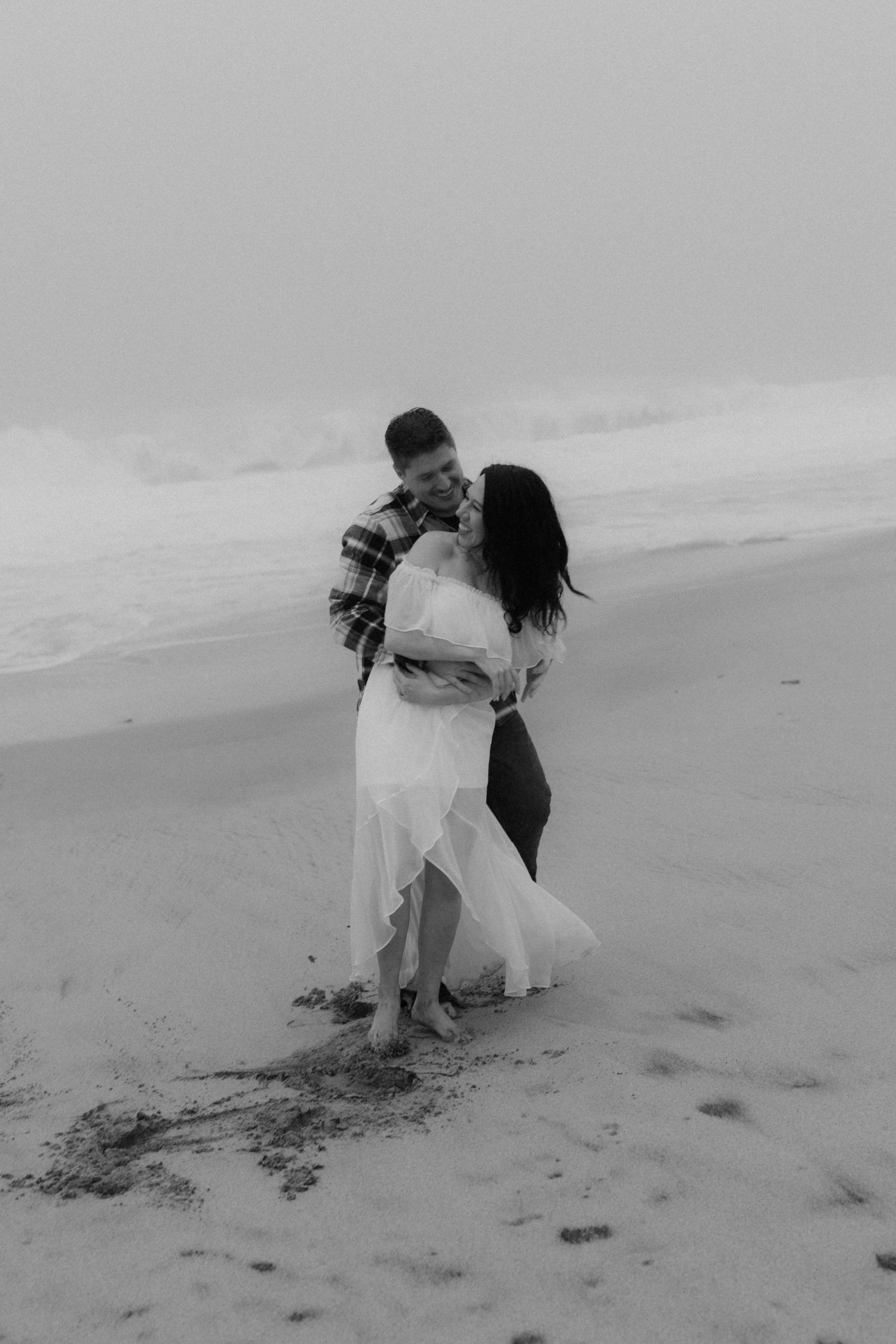 A black and white photo captures a playful moment on the beach with waves in the background.