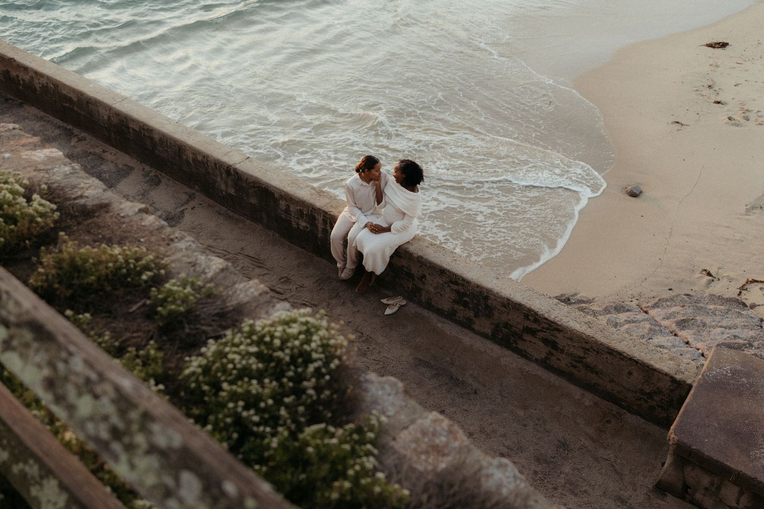 A scenic coastal walkway with waves crashing against rocks and small figures walking along the path by the ocean.