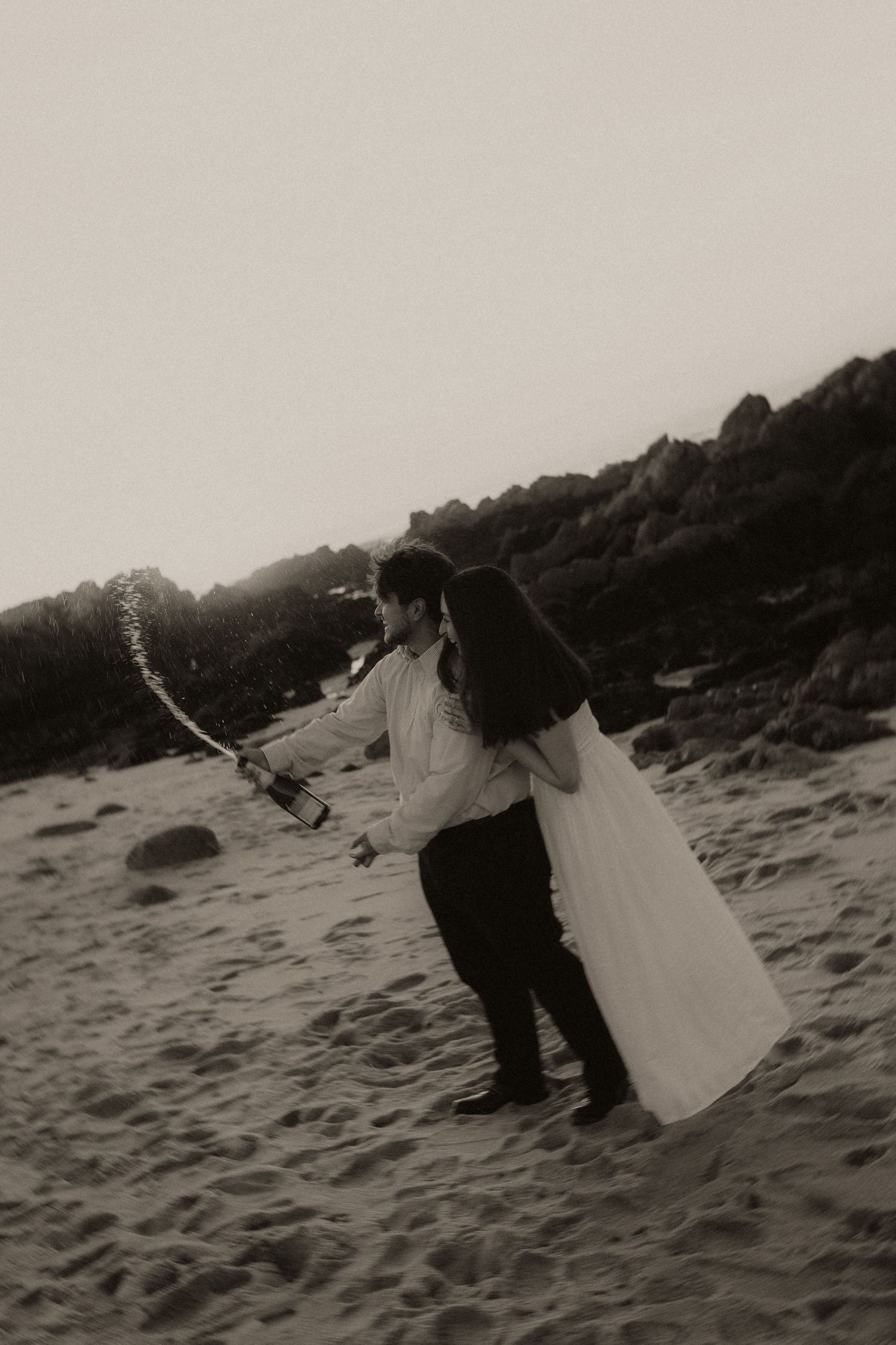 A sequence of black and white photos showing someone playing with a white sheet on a sandy beach.