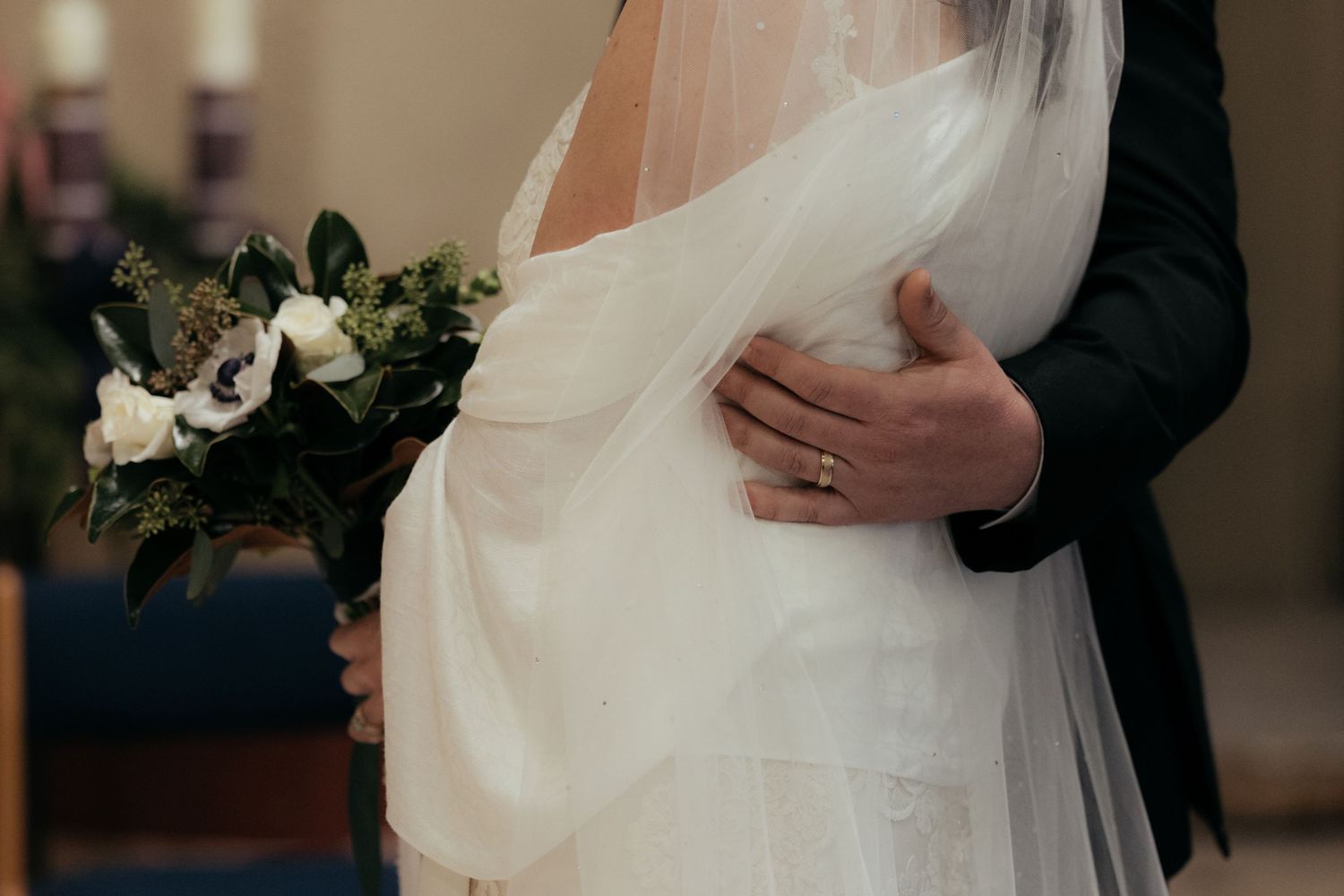 Intimate moment captured showing wedding bouquet and embrace during ceremony.