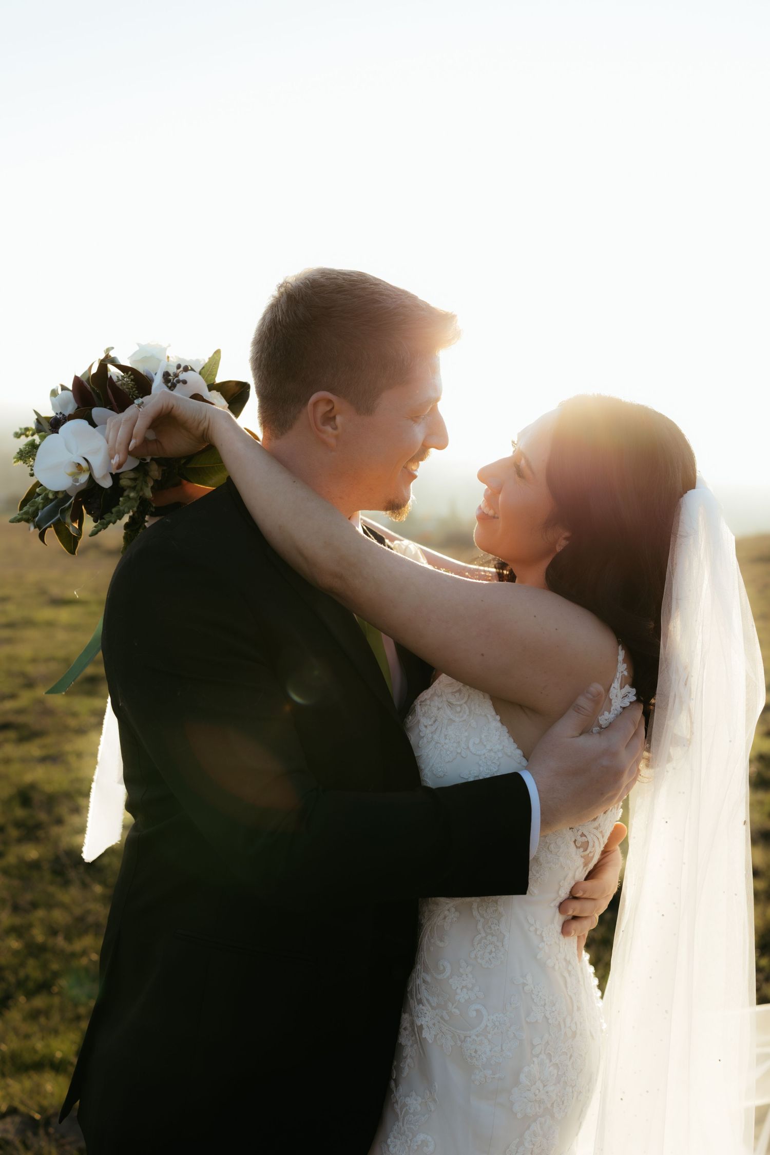 A romantic wedding couple embraces on a hilltop during golden hour sunset.