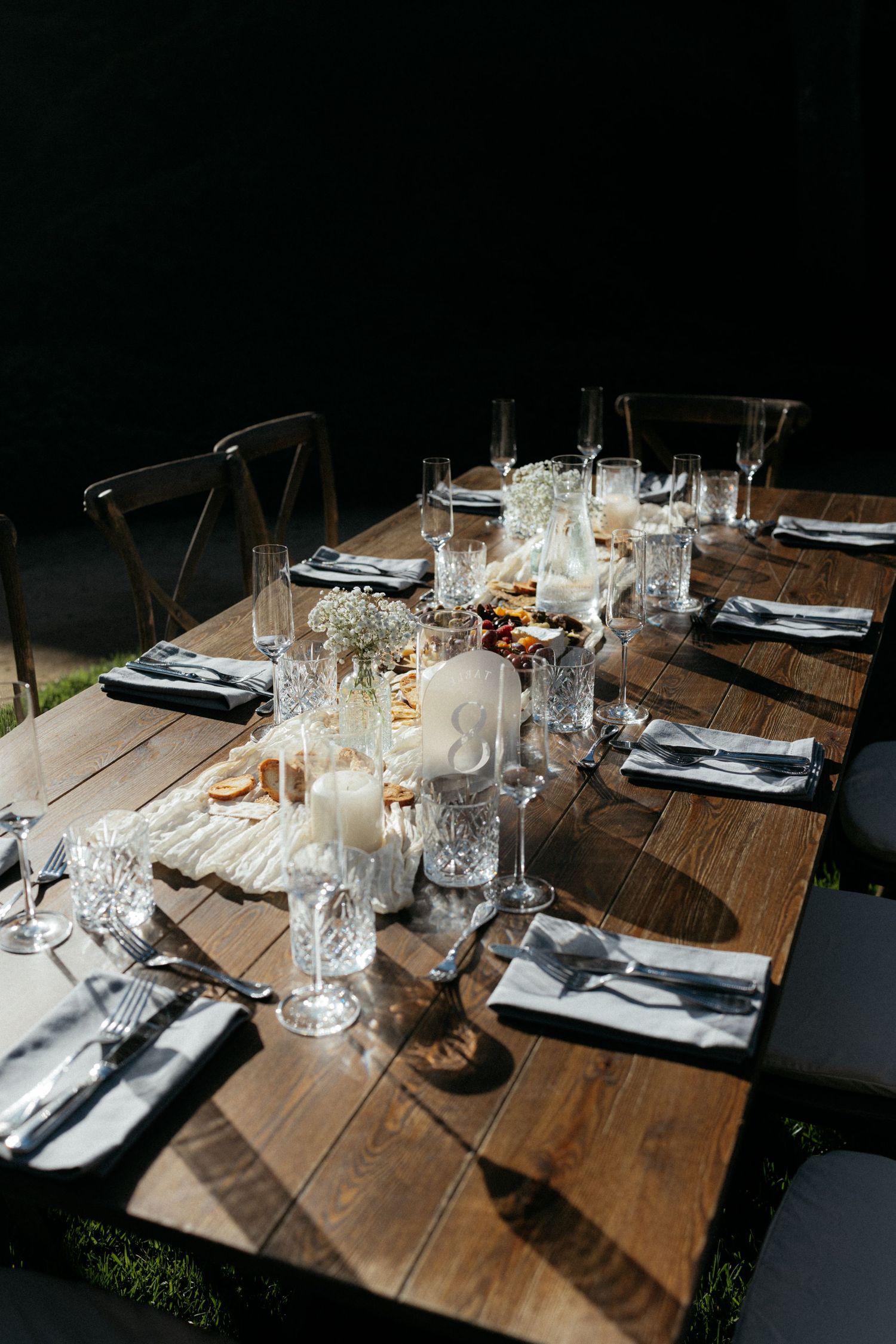 Elegant rustic wooden reception table with crystal glassware, candles, and white floral centerpieces.