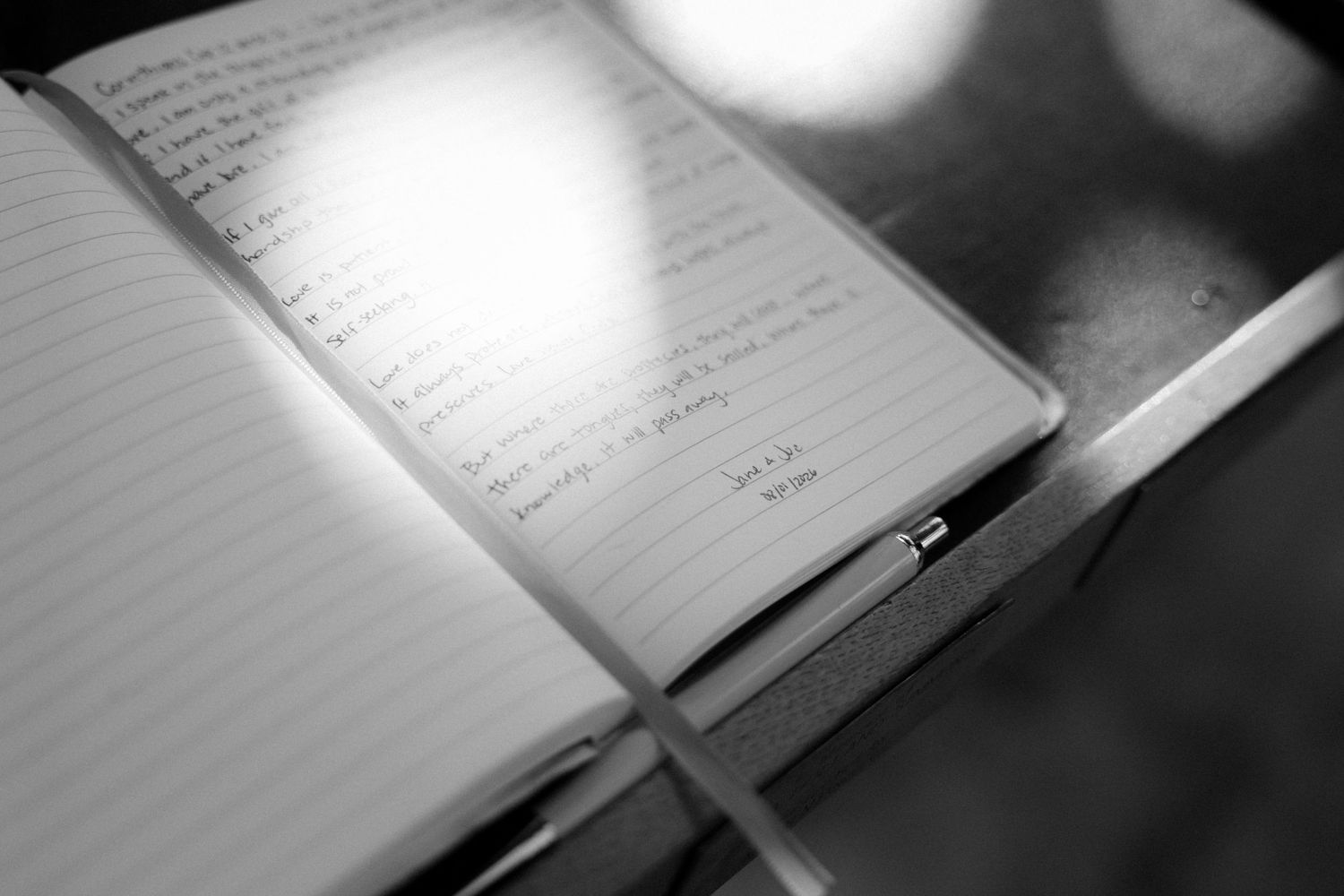Black and white photo of an open journal with handwritten notes and a pen resting on lined pages.