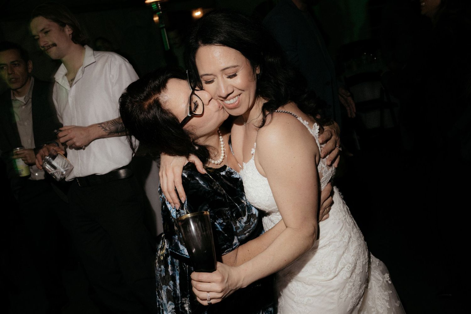 Wedding guests dancing and embracing on a dark dance floor.