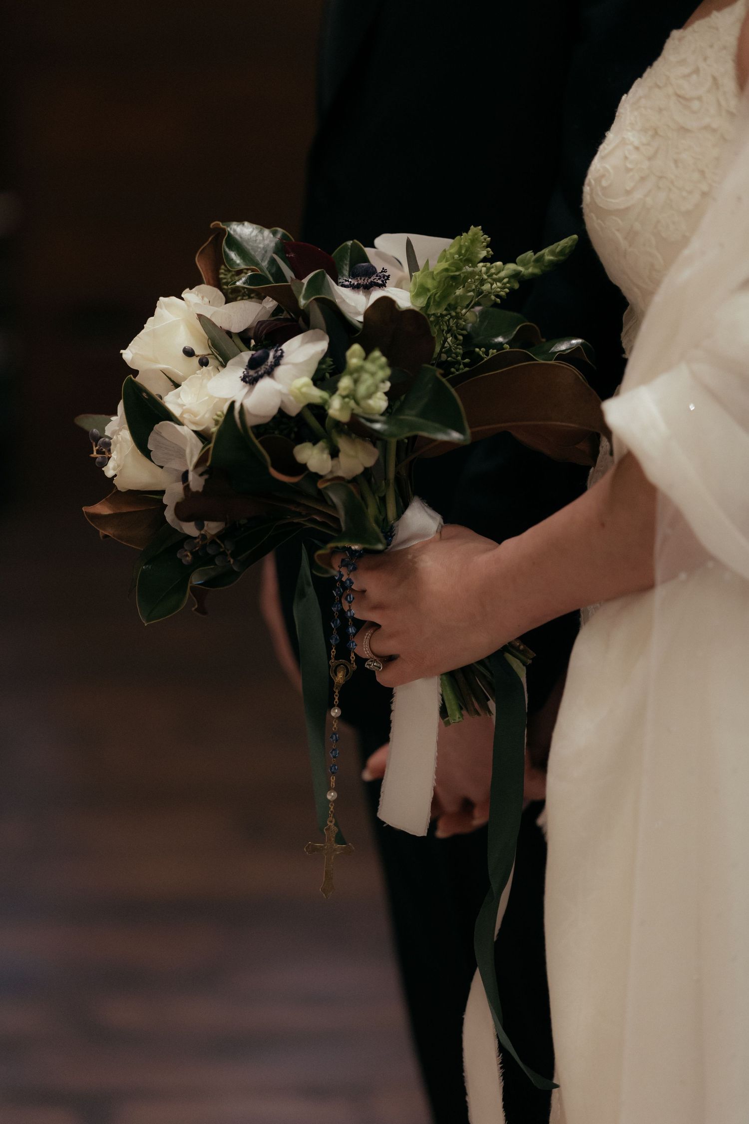 Close-up of wedding couple holding elegant white and green floral bouquets during ceremony.
