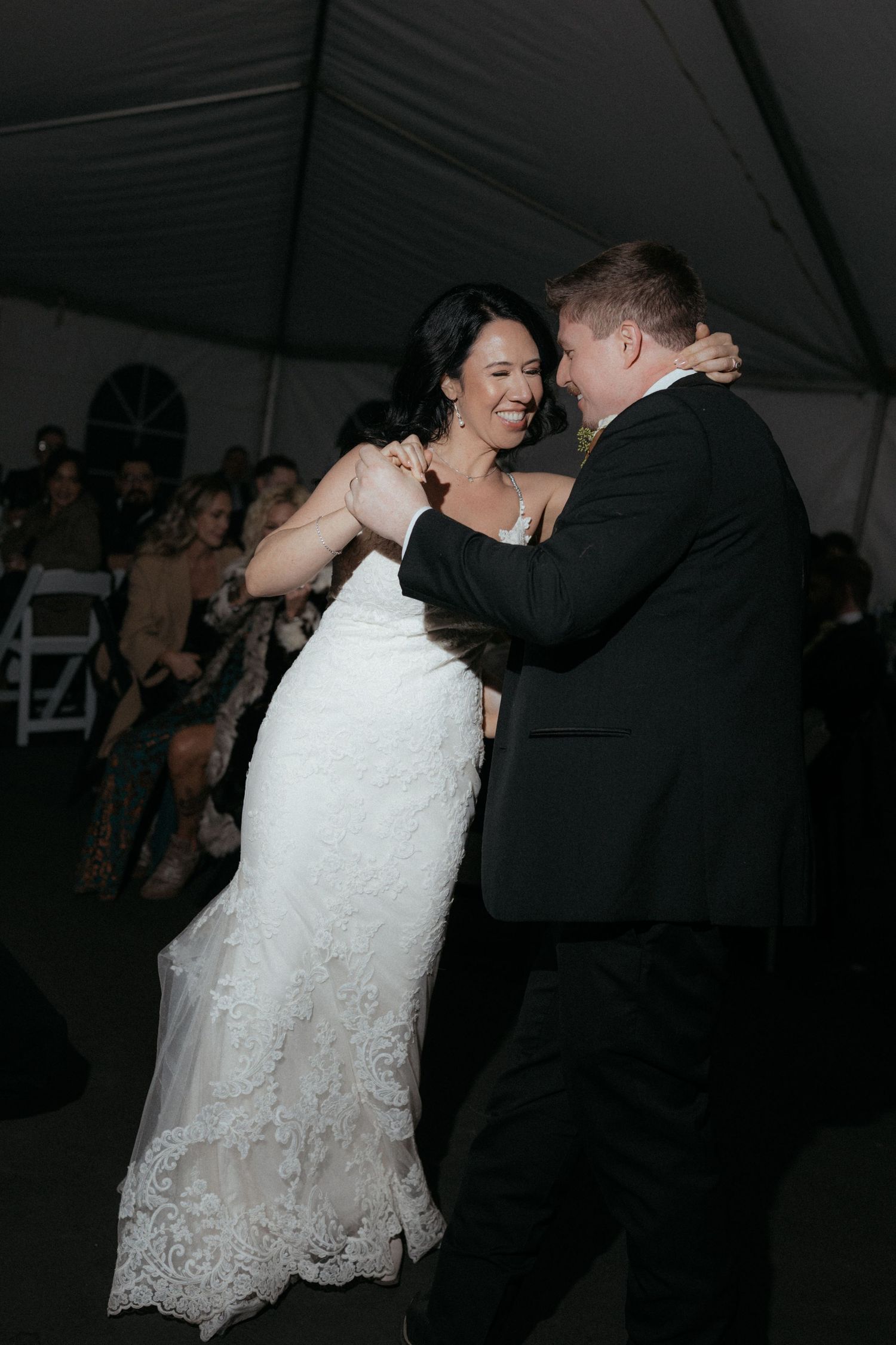 Couple dancing at a wedding reception with bride in white lace dress and groom in black suit.