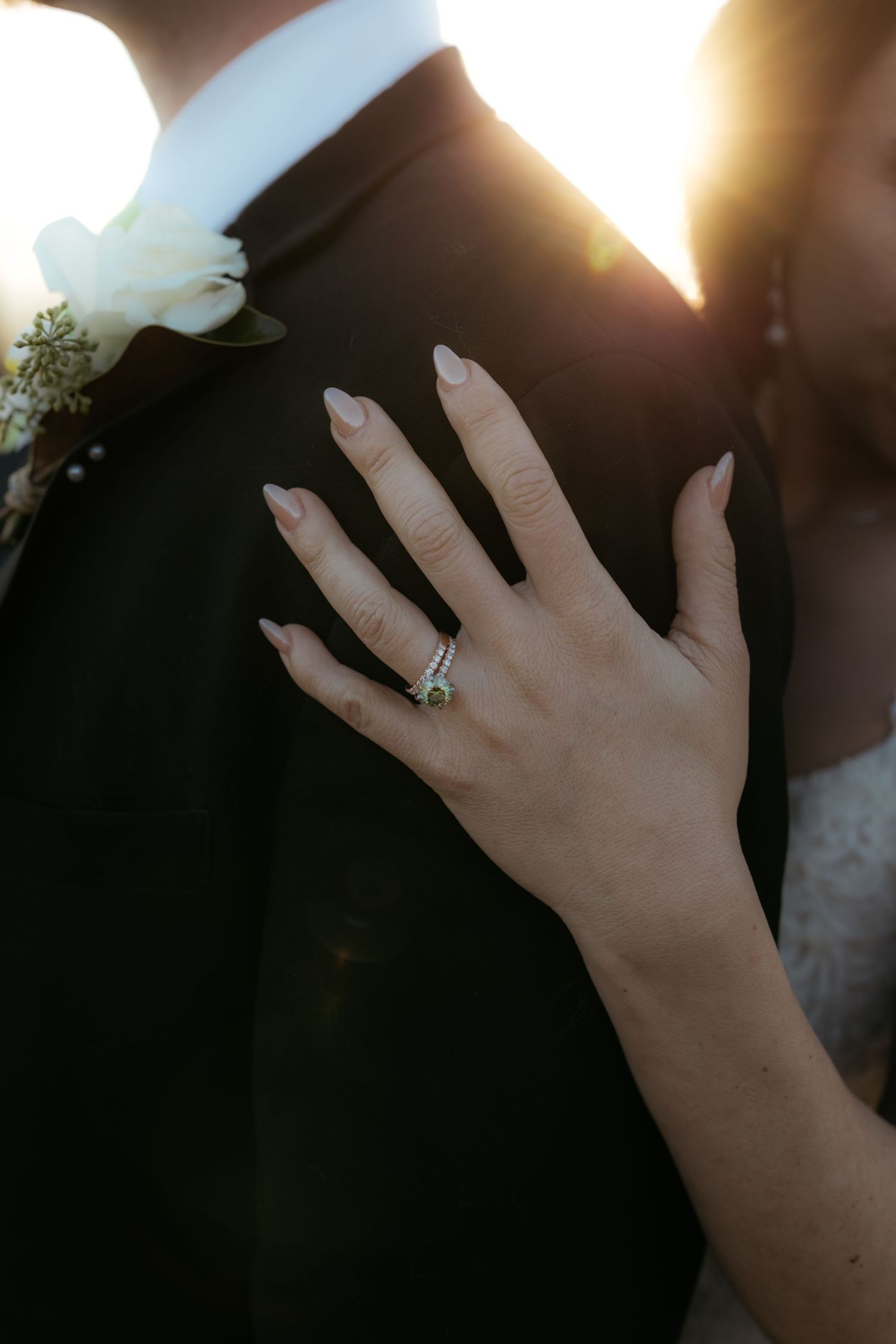 Delicate hands with an engagement ring shown against sunlit backdrop during a wedding ceremony.