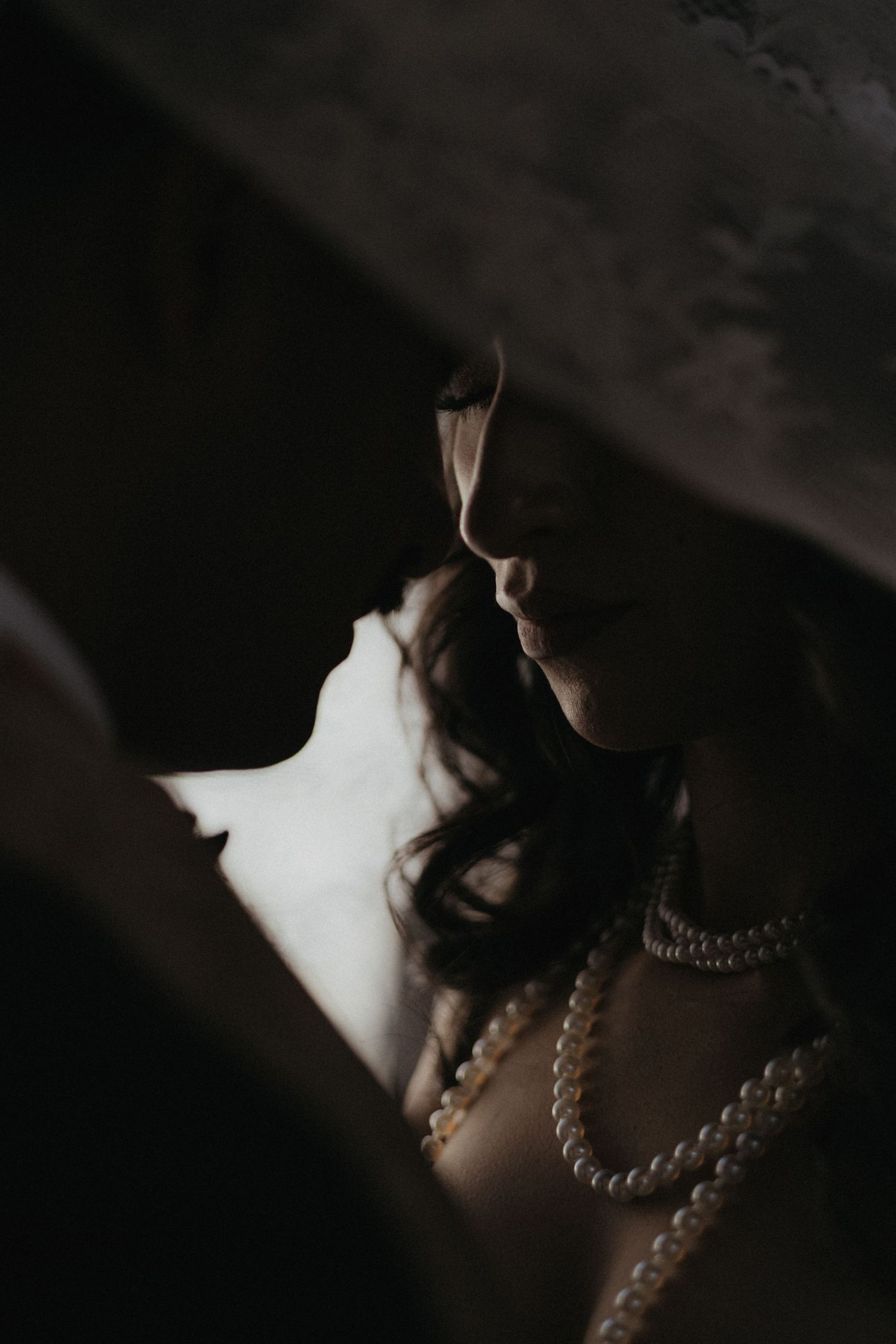 A dramatic close-up portrait of a bride wearing pearls in moody lighting.