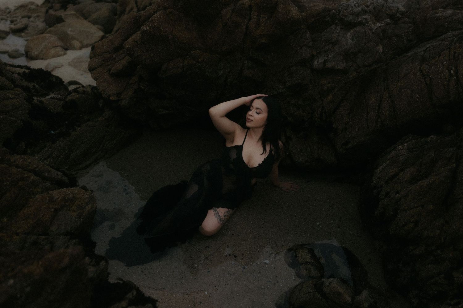 Artistic pose captured among shadowy coastal rock formations.