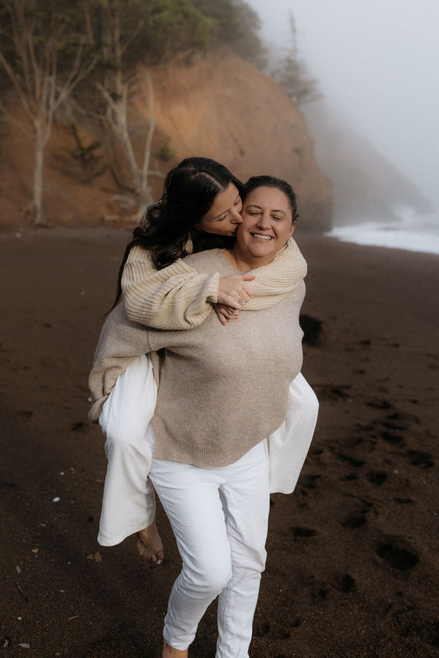 A joyful moment shared between two people embracing on a foggy beach with cliffs in the background.