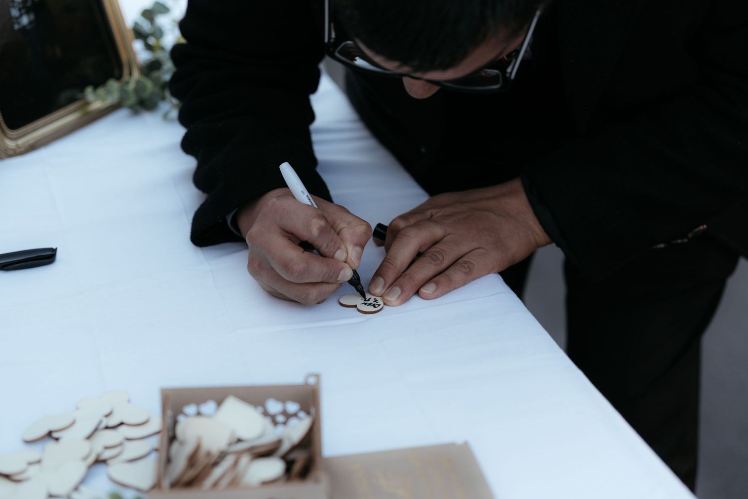 Hands signing a wedding guestbook on a white surface during a reception.