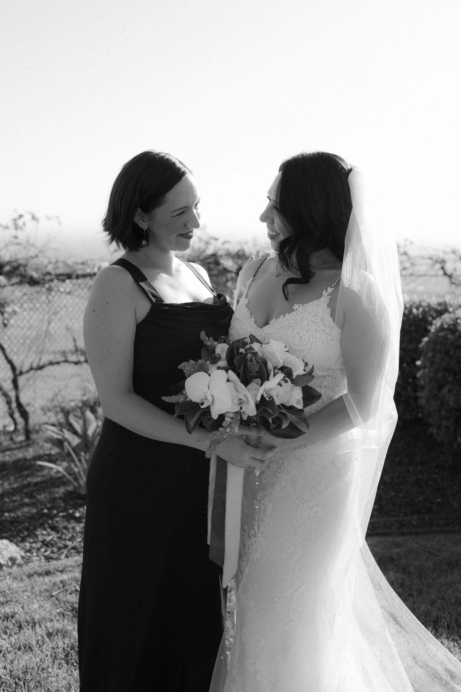 Black and white photo of a tender moment between bride and bridesmaid during an outdoor wedding celebration.