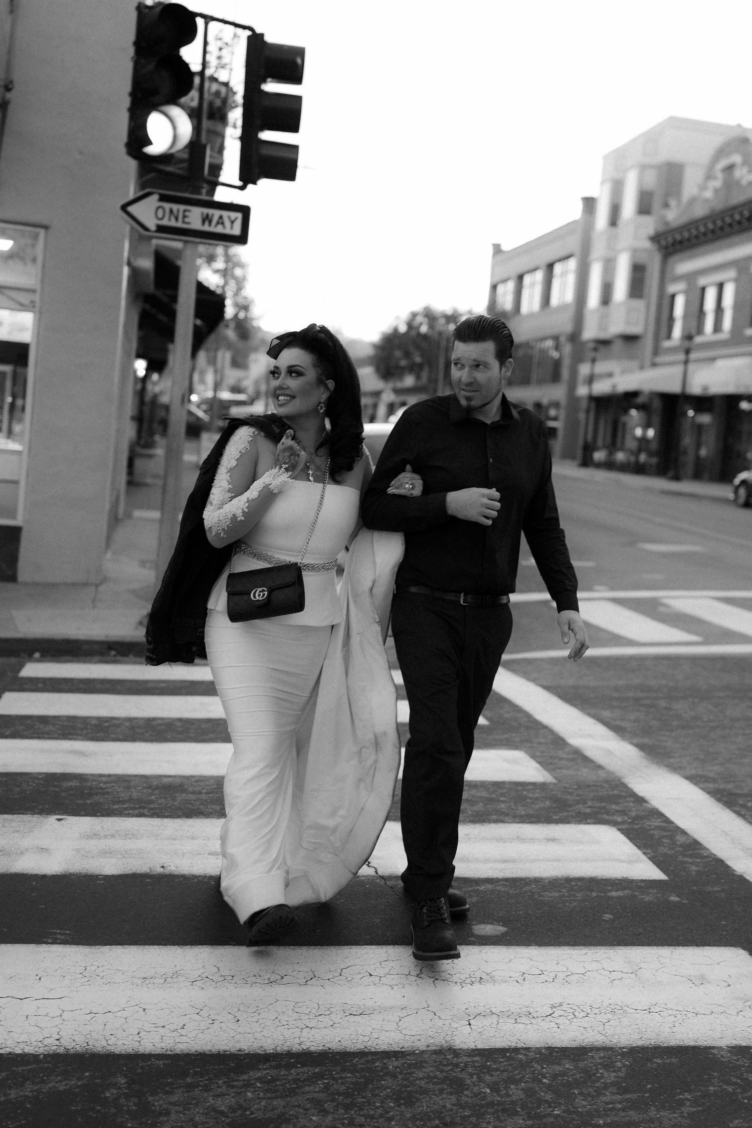 A couple walks together on a city street with the bride's dress trailing behind them.