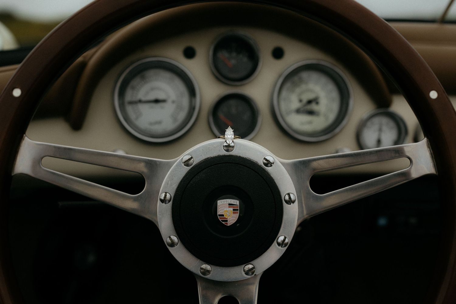 Vintage Porsche steering wheel with classic gauges on dashboard of a retro sports car interior.