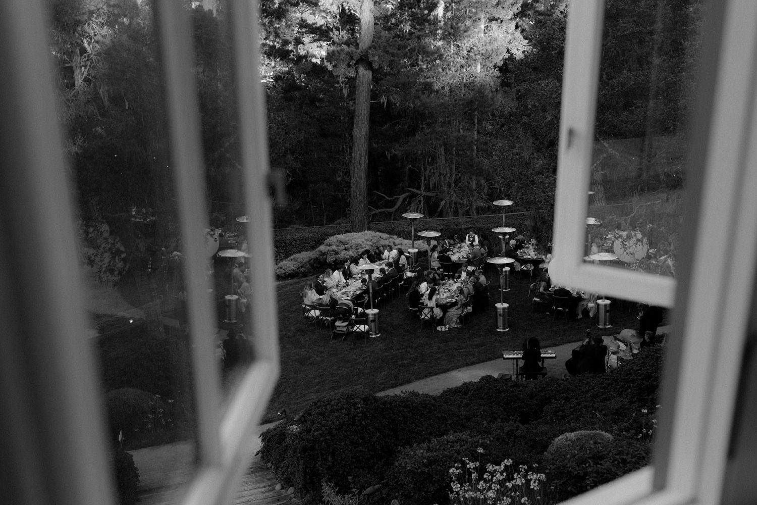 Black and white aerial view of an elegant outdoor garden wedding reception with guests seated among lush trees.