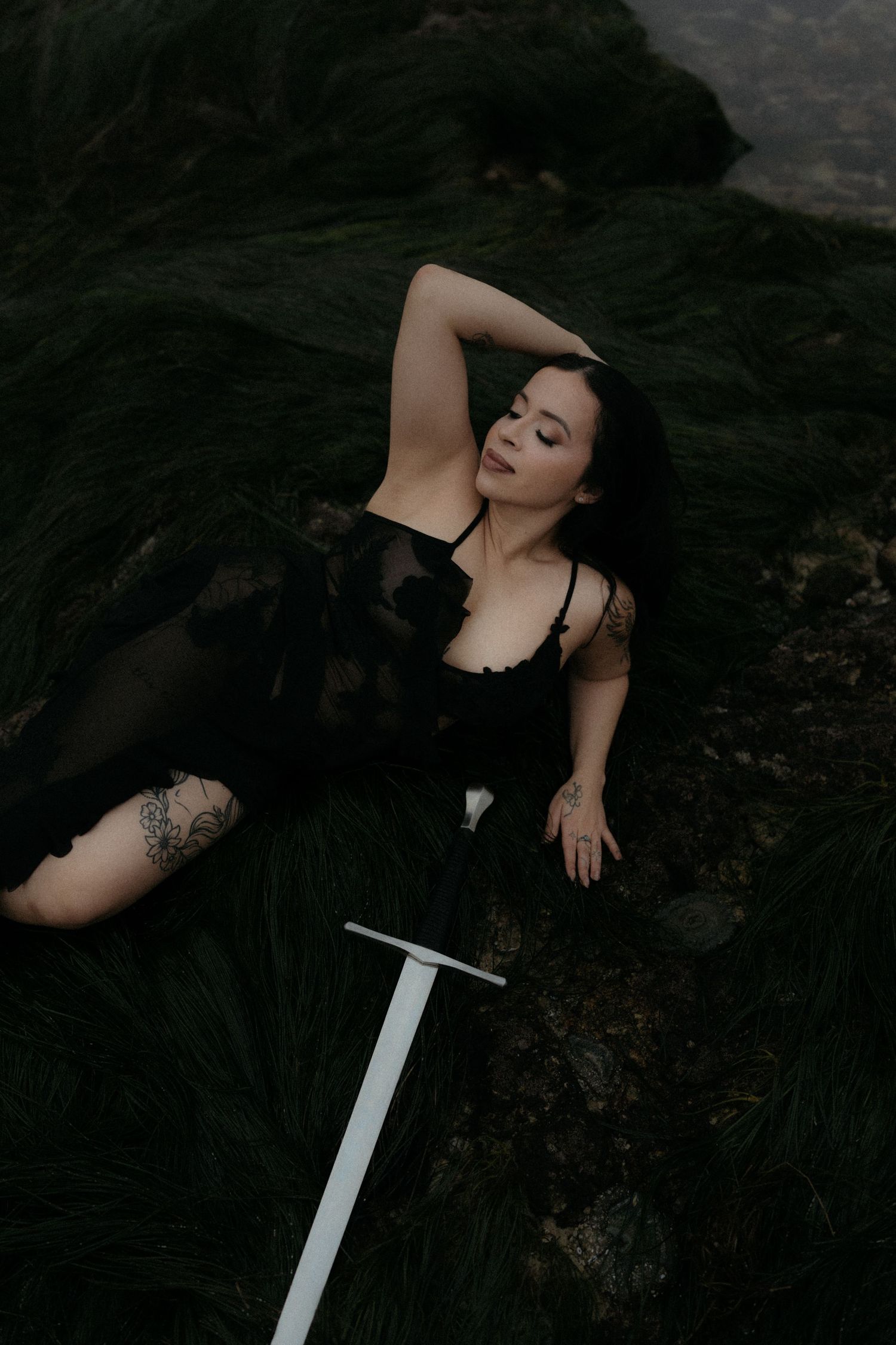 Dark atmospheric portrait with figure in black dress posed with a white sword prop.