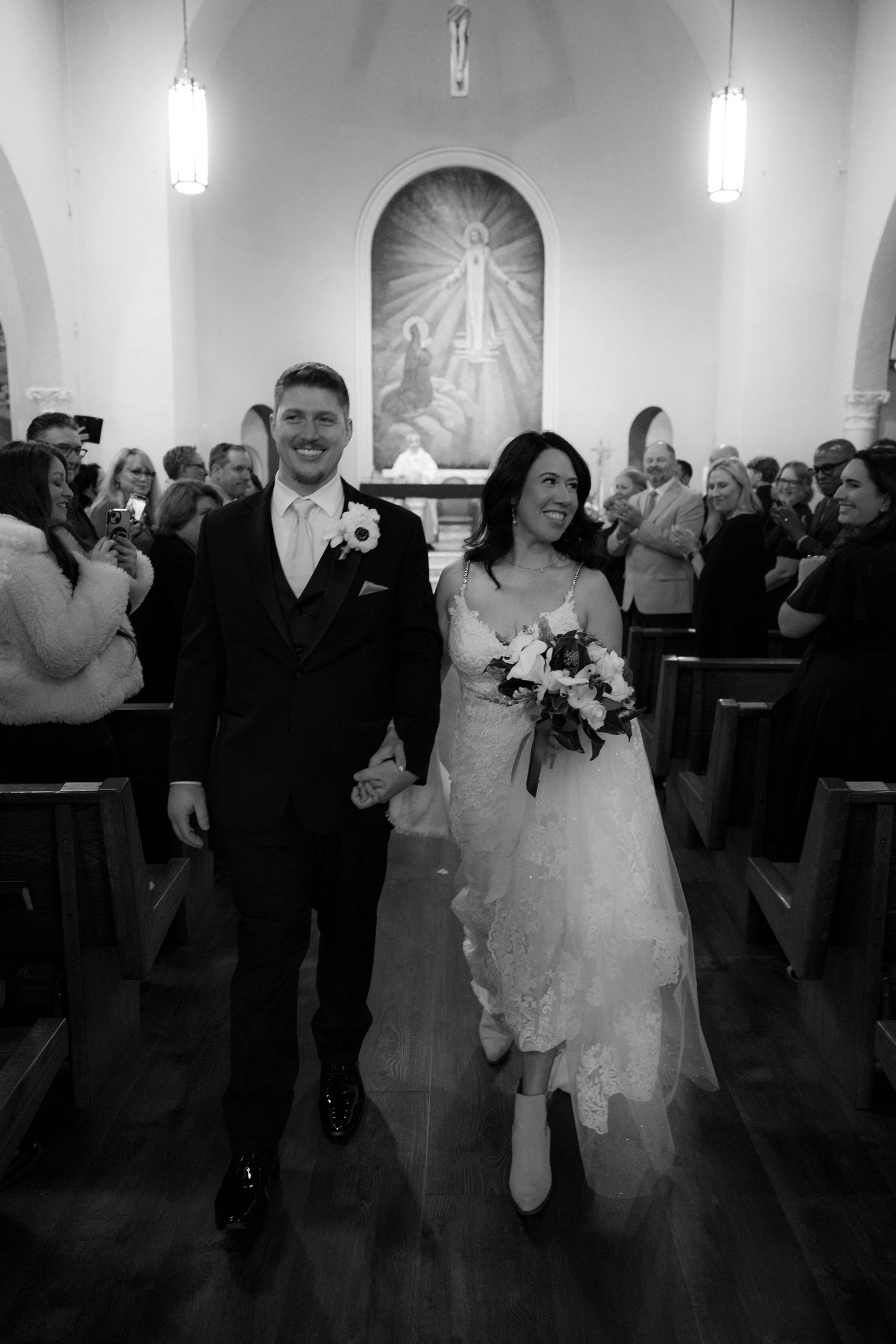 A joyful wedding celebration captured in black and white as newlyweds walk down the aisle after their ceremony.
