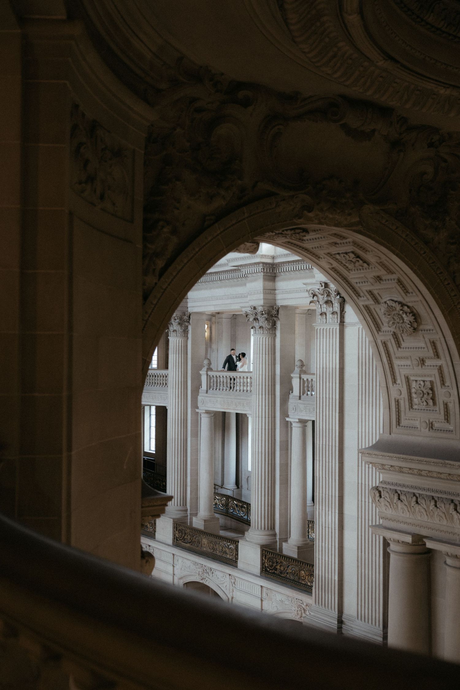 Ornate classical architecture with white columns and arches viewed through a decorative stone archway.