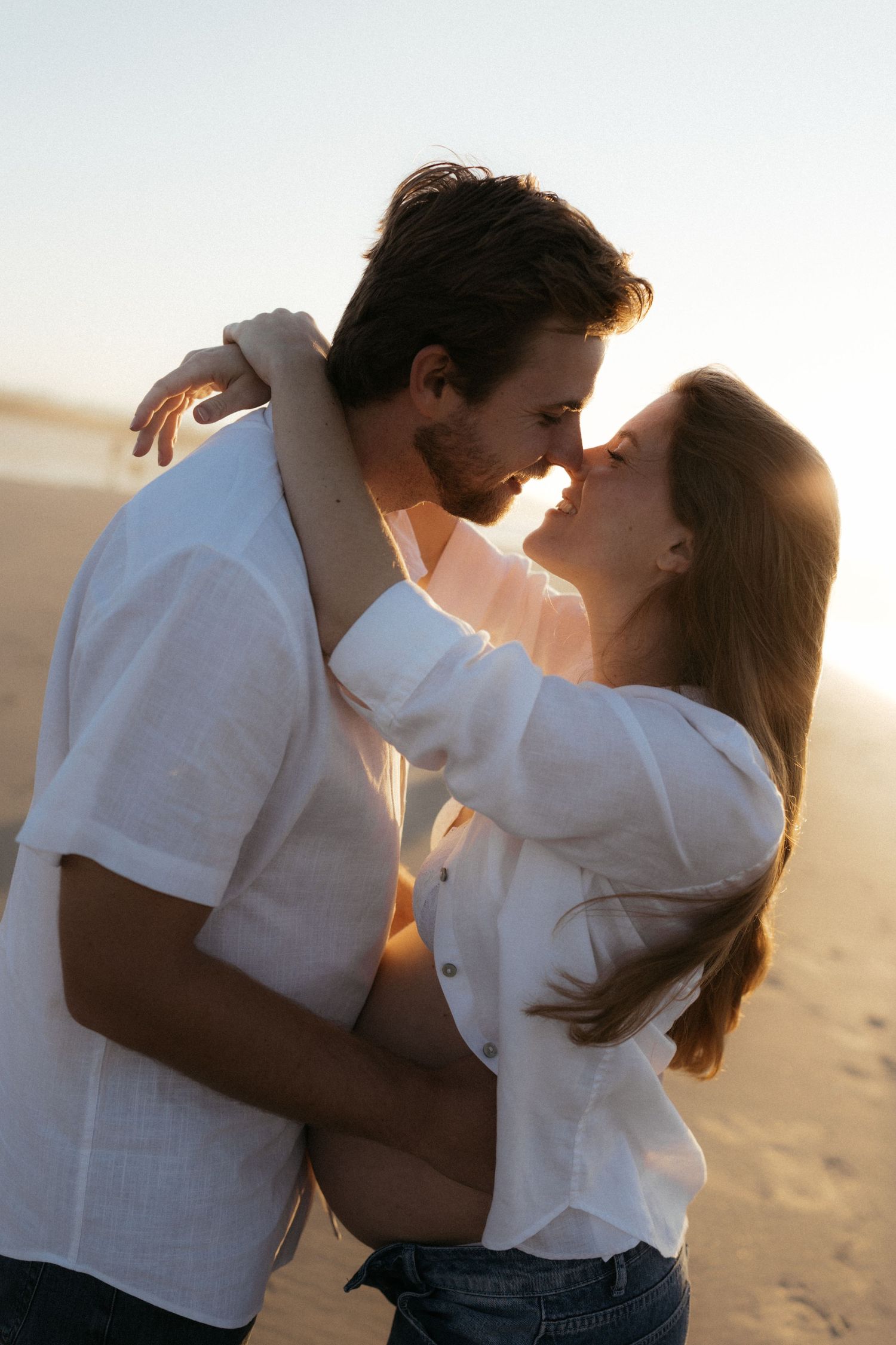 Romantic couple embracing and about to kiss on a sun-drenched beach at golden hour.