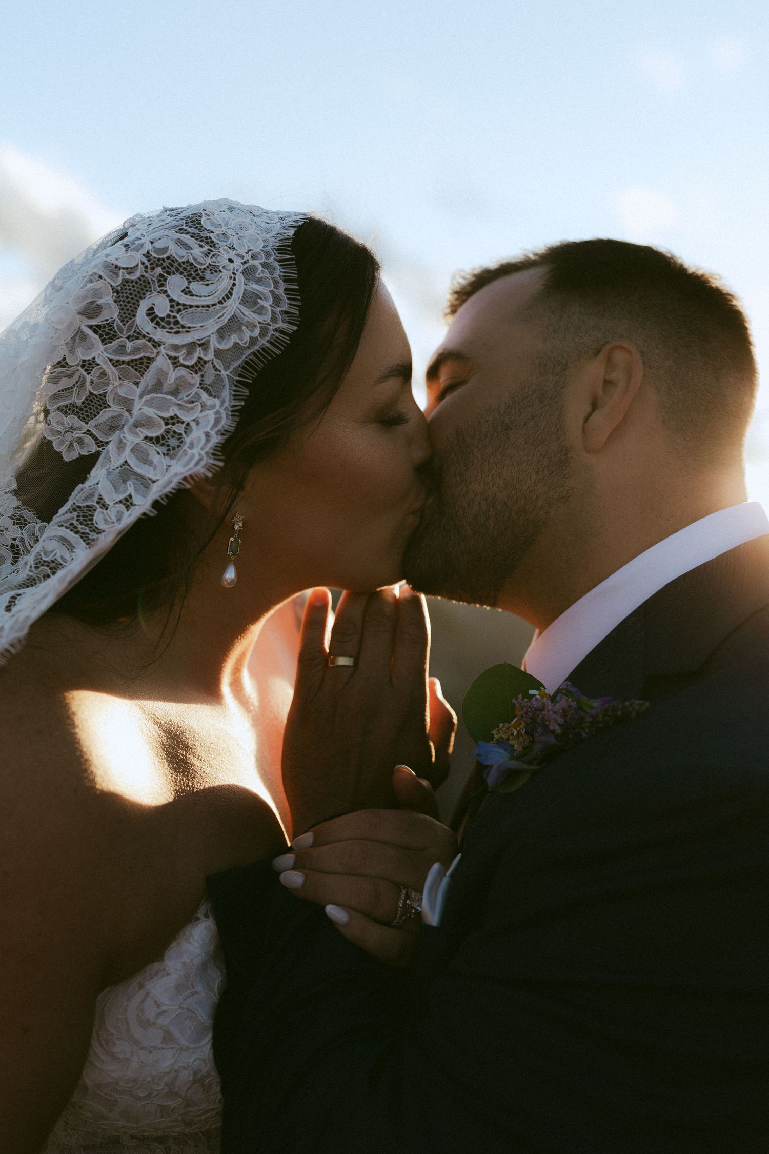 Bride and groom share a romantic kiss at golden hour, bride wearing lace veil.
