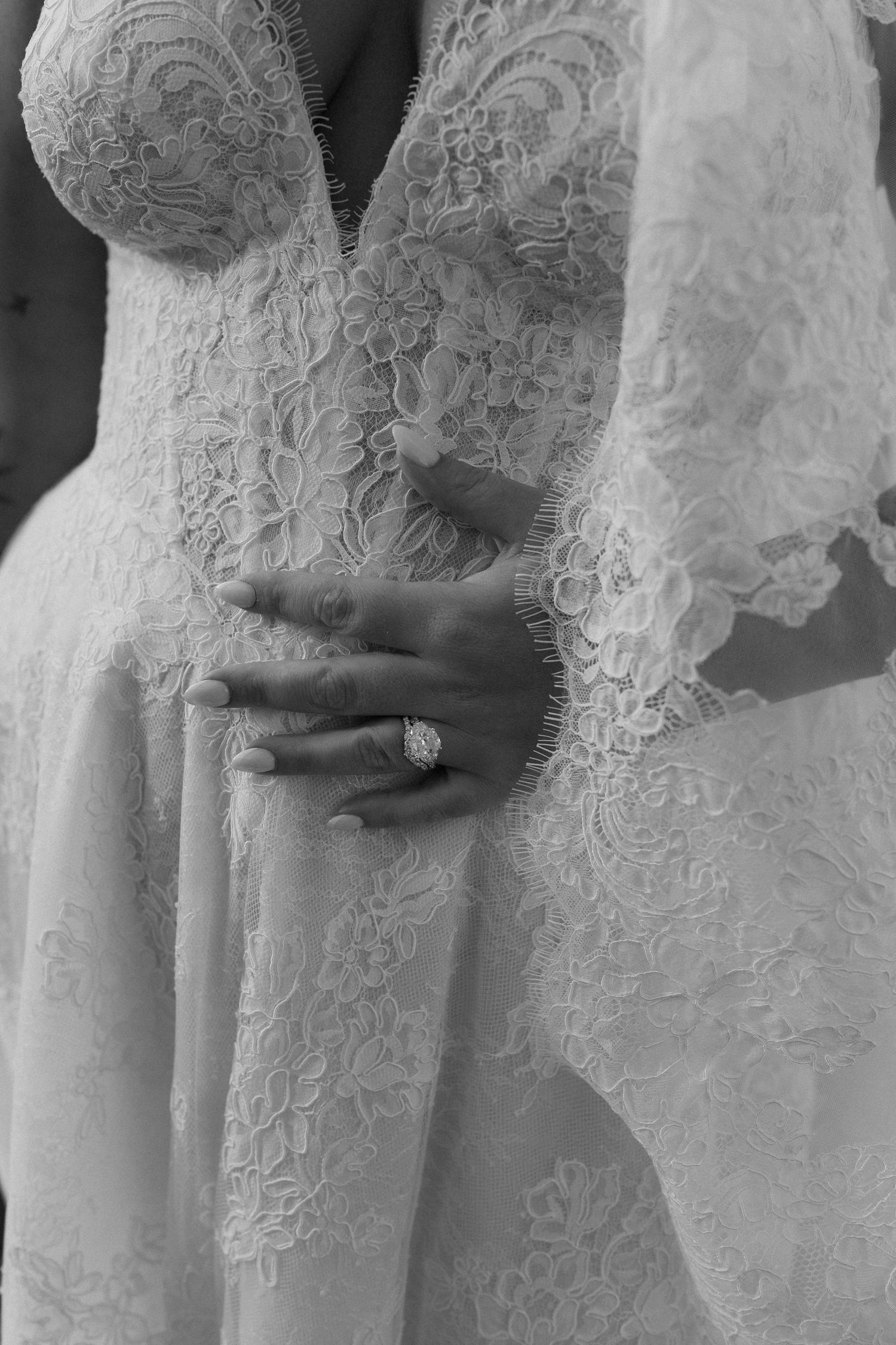 Black and white close-up of bride in lace wedding gown showcasing elegant diamond engagement ring.