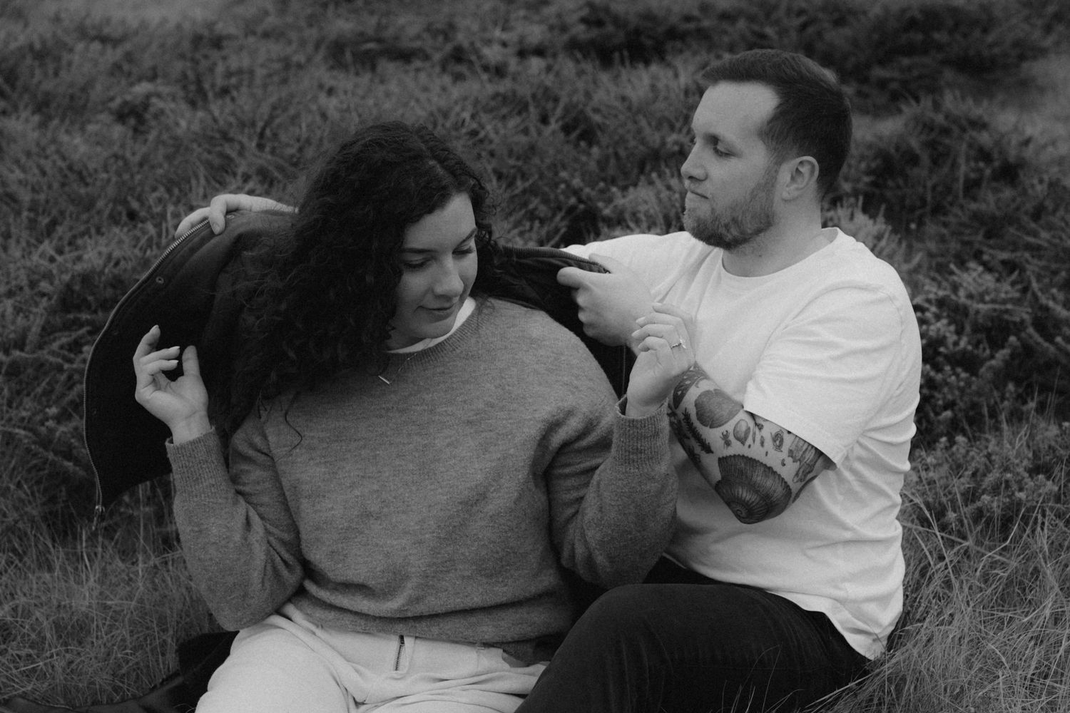 A couple shares a playful moment together outdoors in black and white photography.
