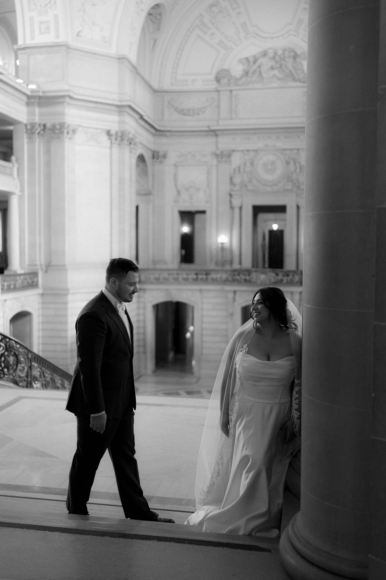 Black and white wedding photos captured in a grand marble hallway with classical columns and architectural details.