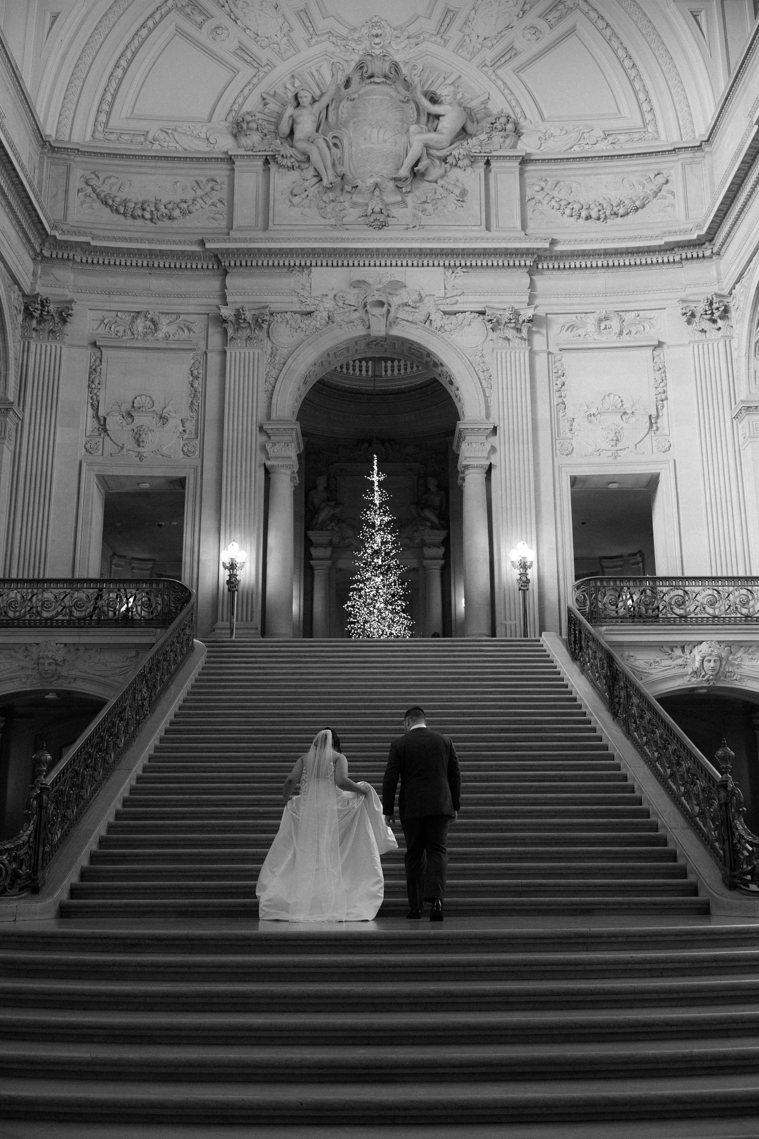 A grand staircase in an ornate building with a Christmas tree visible at the top of the stairs.