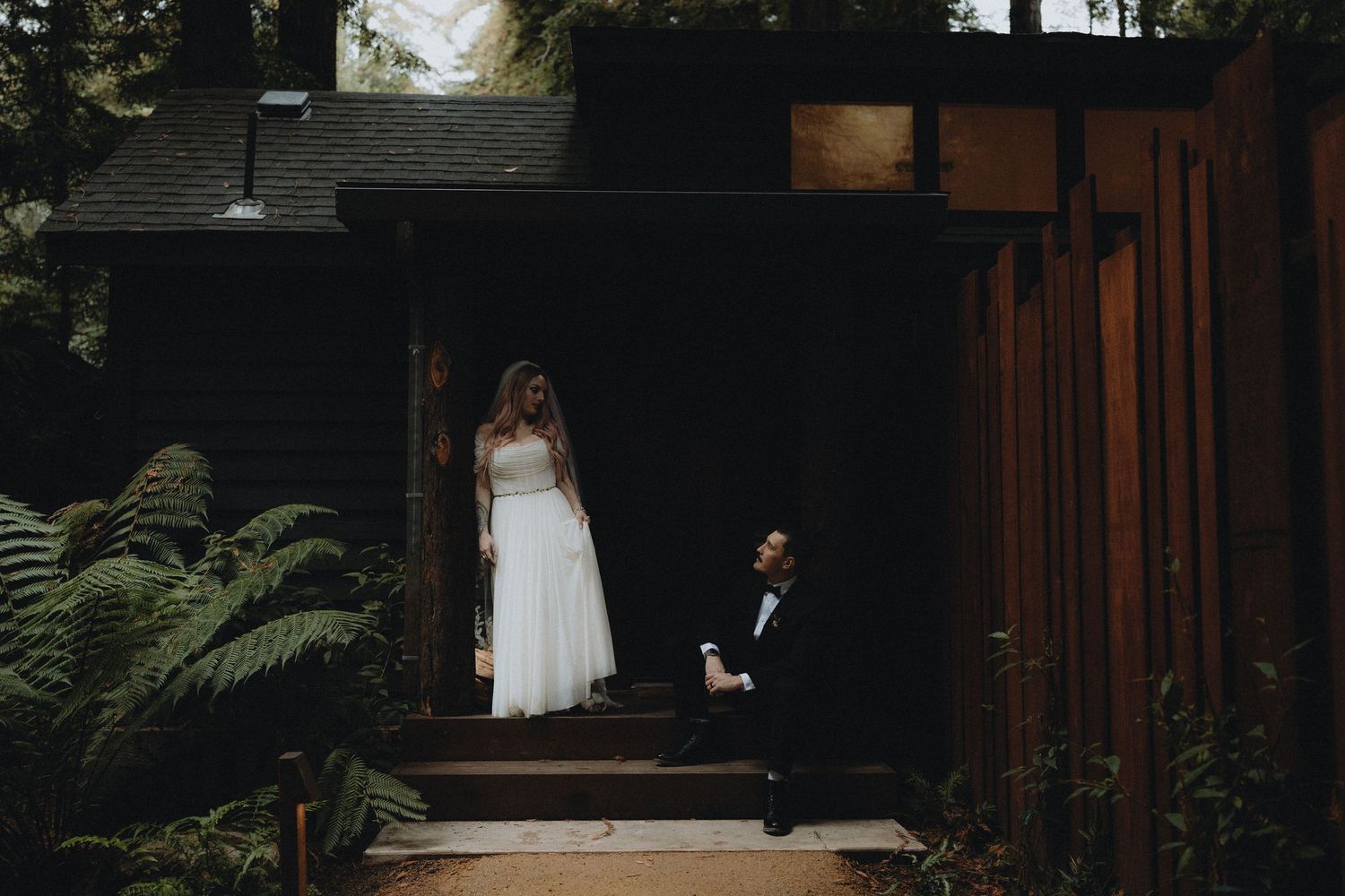 A couple shares a romantic moment on a rustic wooden porch surrounded by lush greenery and ferns.
