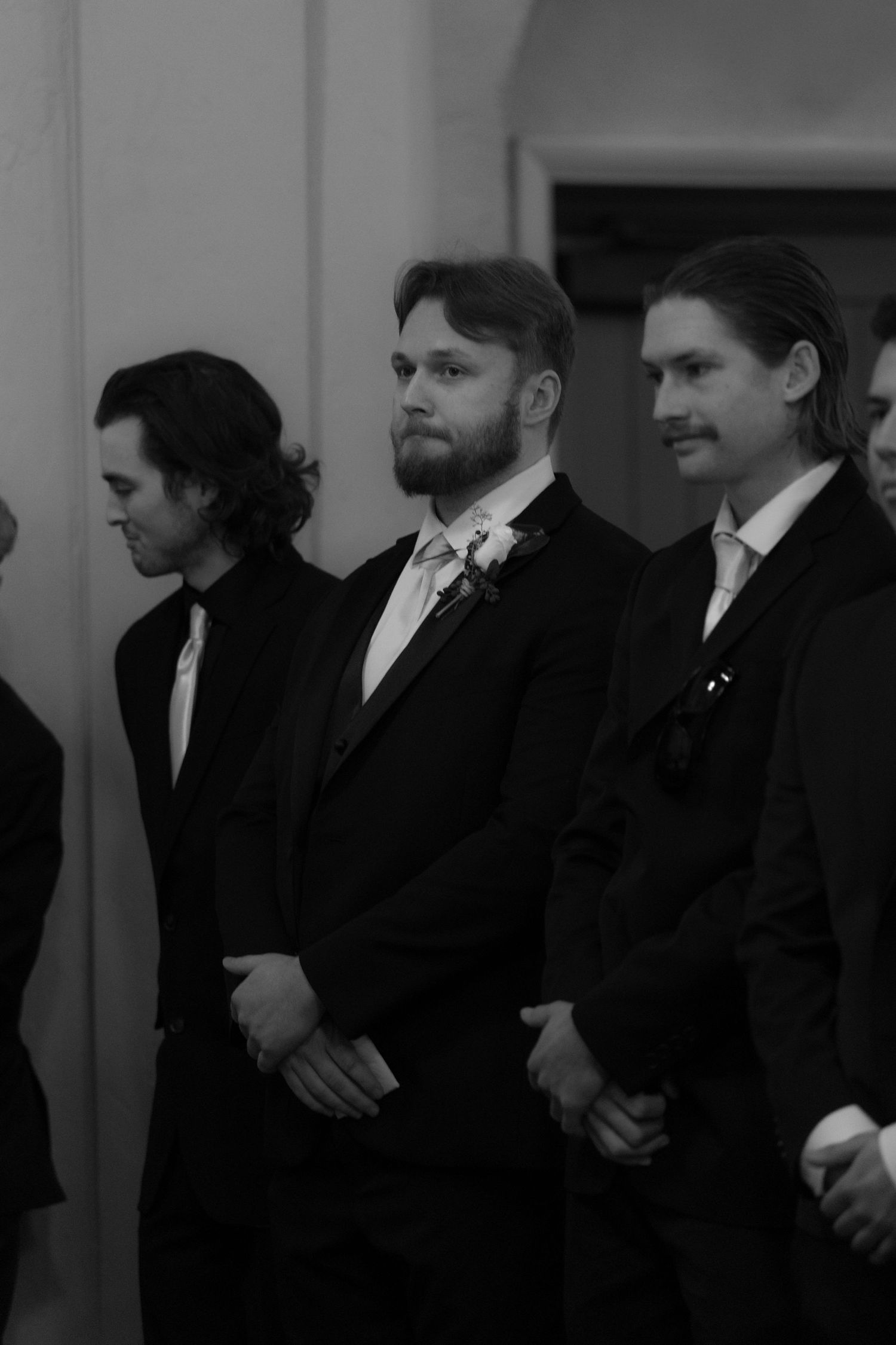 A row of groomsmen in black suits and ties stand together during a formal wedding ceremony.