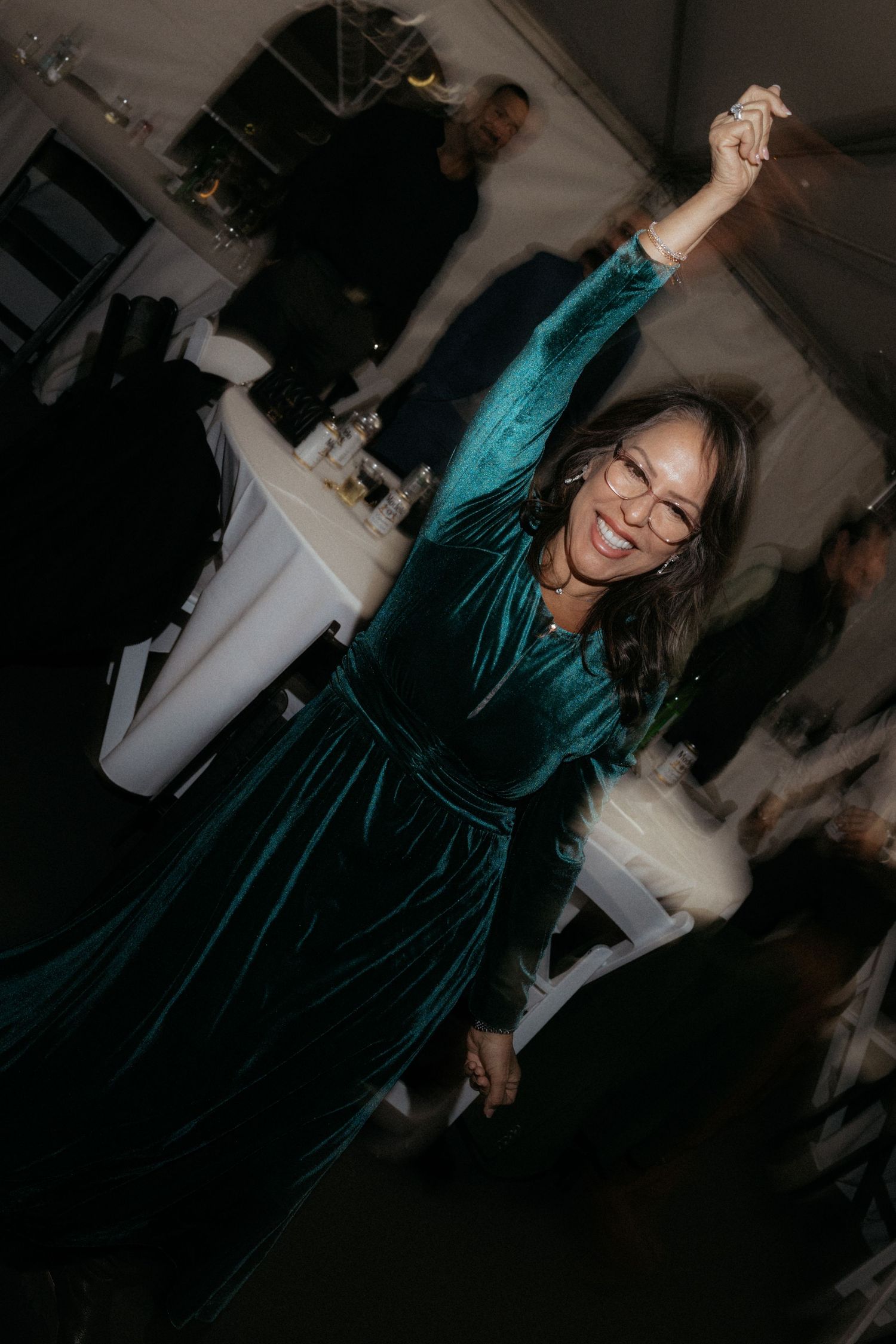 A guest in an emerald velvet dress dances joyfully at an evening celebration.