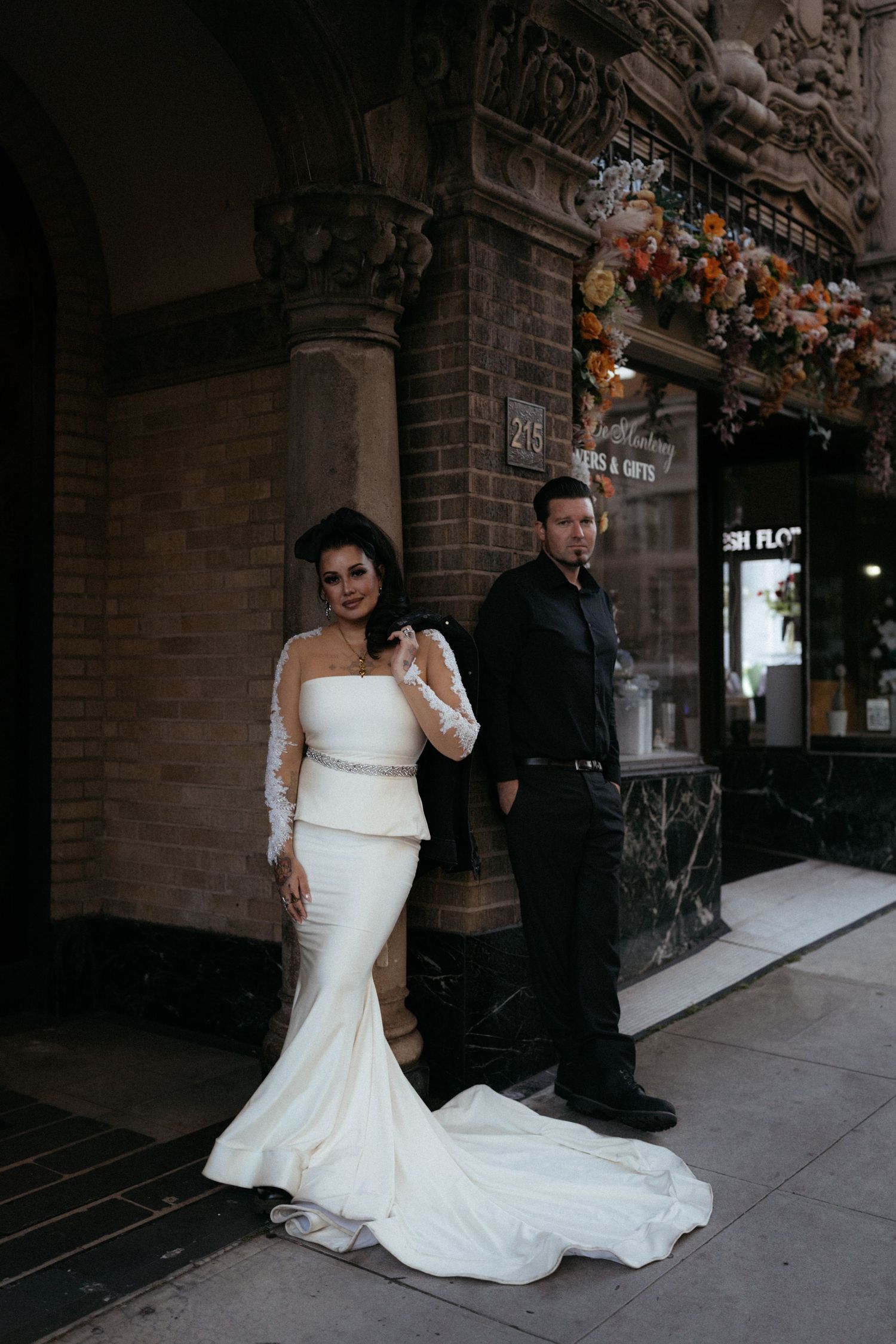 A couple poses outside a brick building, with the bride wearing a flowing white mermaid wedding dress.