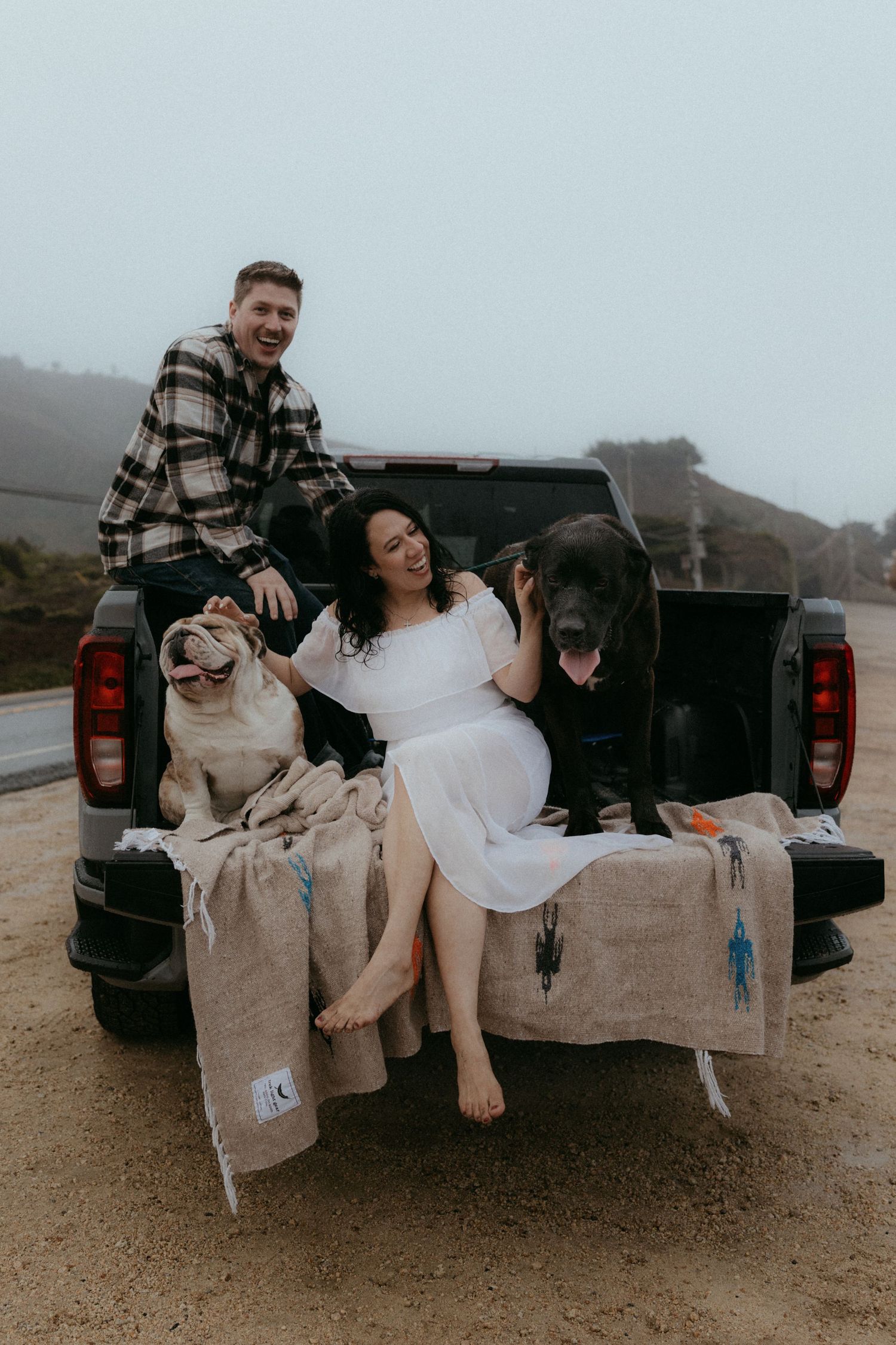 Couple sitting in back of pickup truck on foggy beach sharing intimate moment in moody atmosphere.