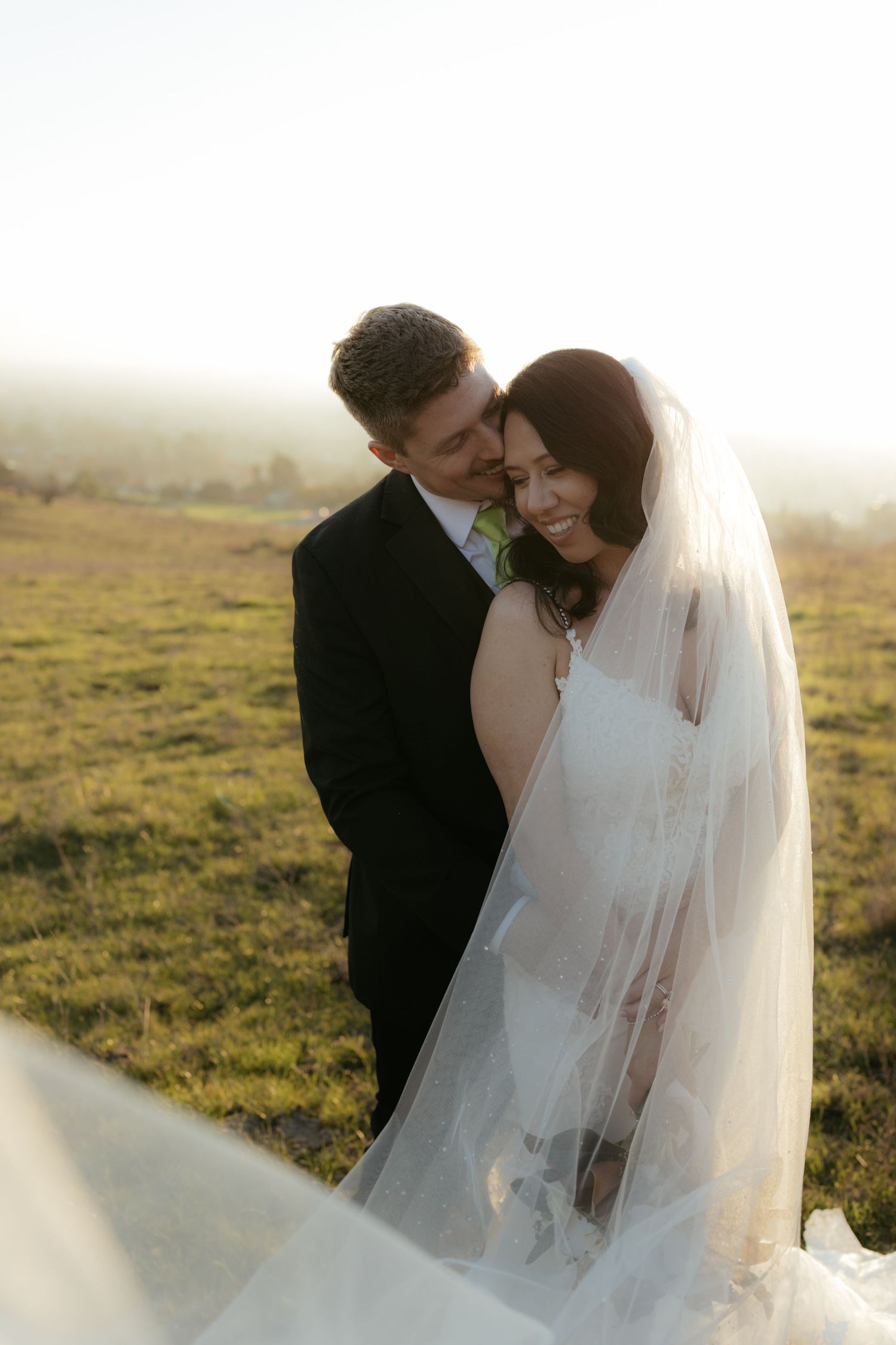 An intimate moment between newlyweds captured in soft golden light on a grassy hillside.
