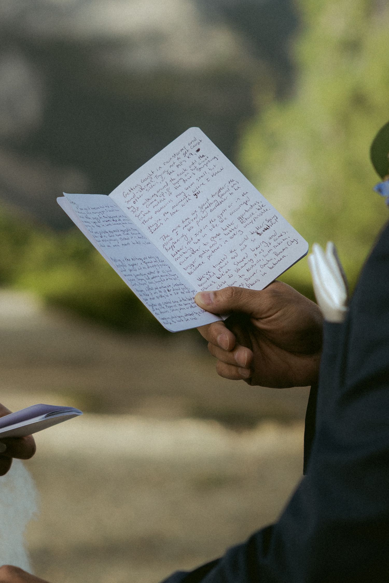 Officiant reading handwritten vows from small notebook during outdoor wedding ceremony.