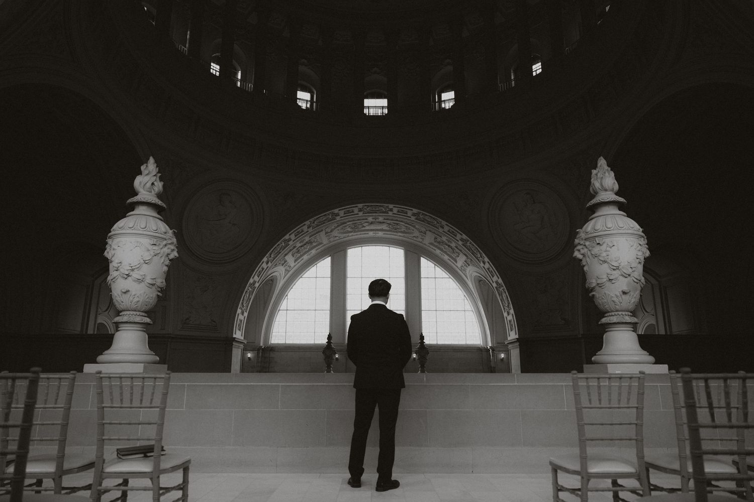 A silhouette stands between classical statues in a grand domed hall.
