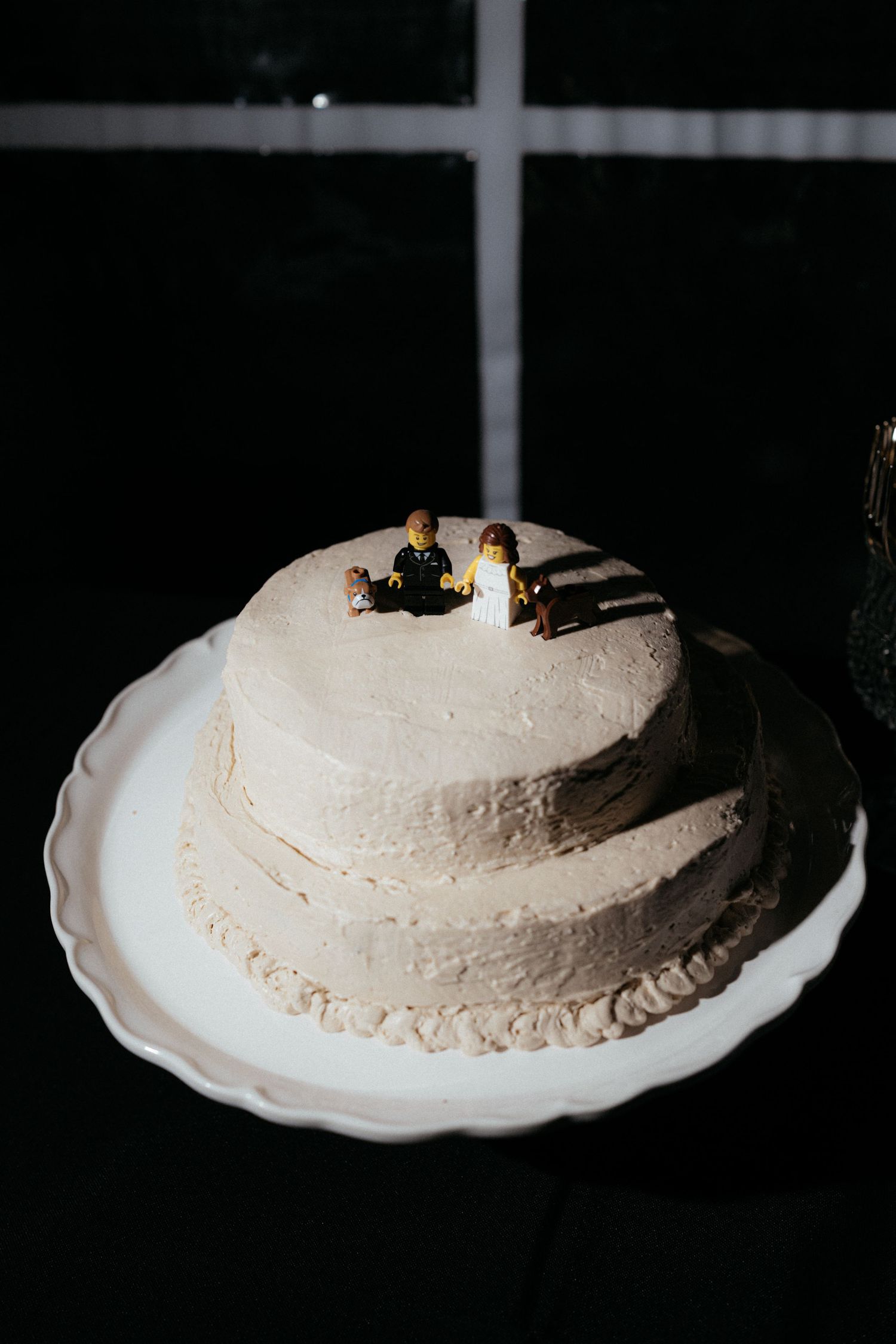 A white frosted cake on a decorative plate photographed in a dark setting.