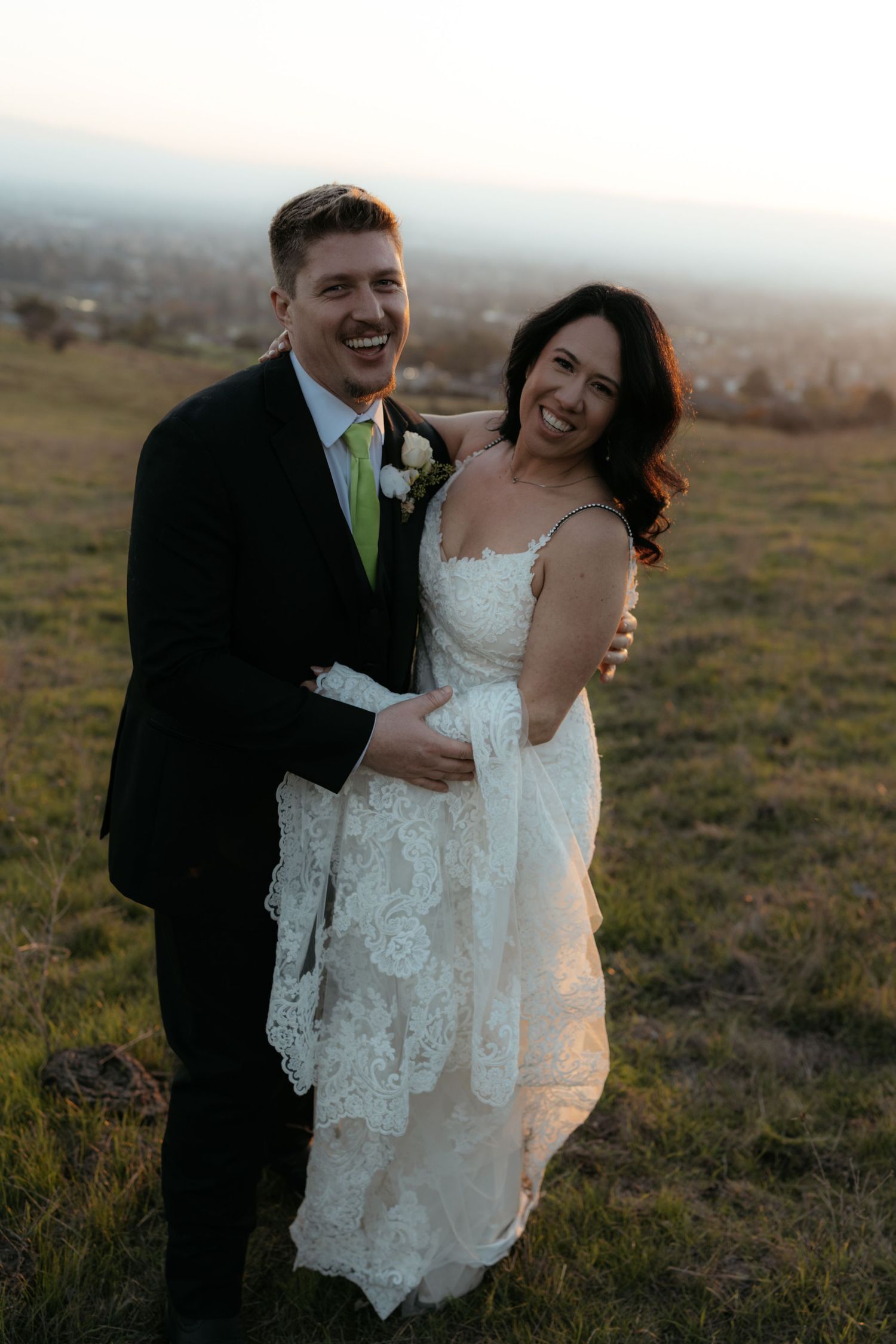 Happy newlyweds sharing a laugh together on a hilltop during golden hour.