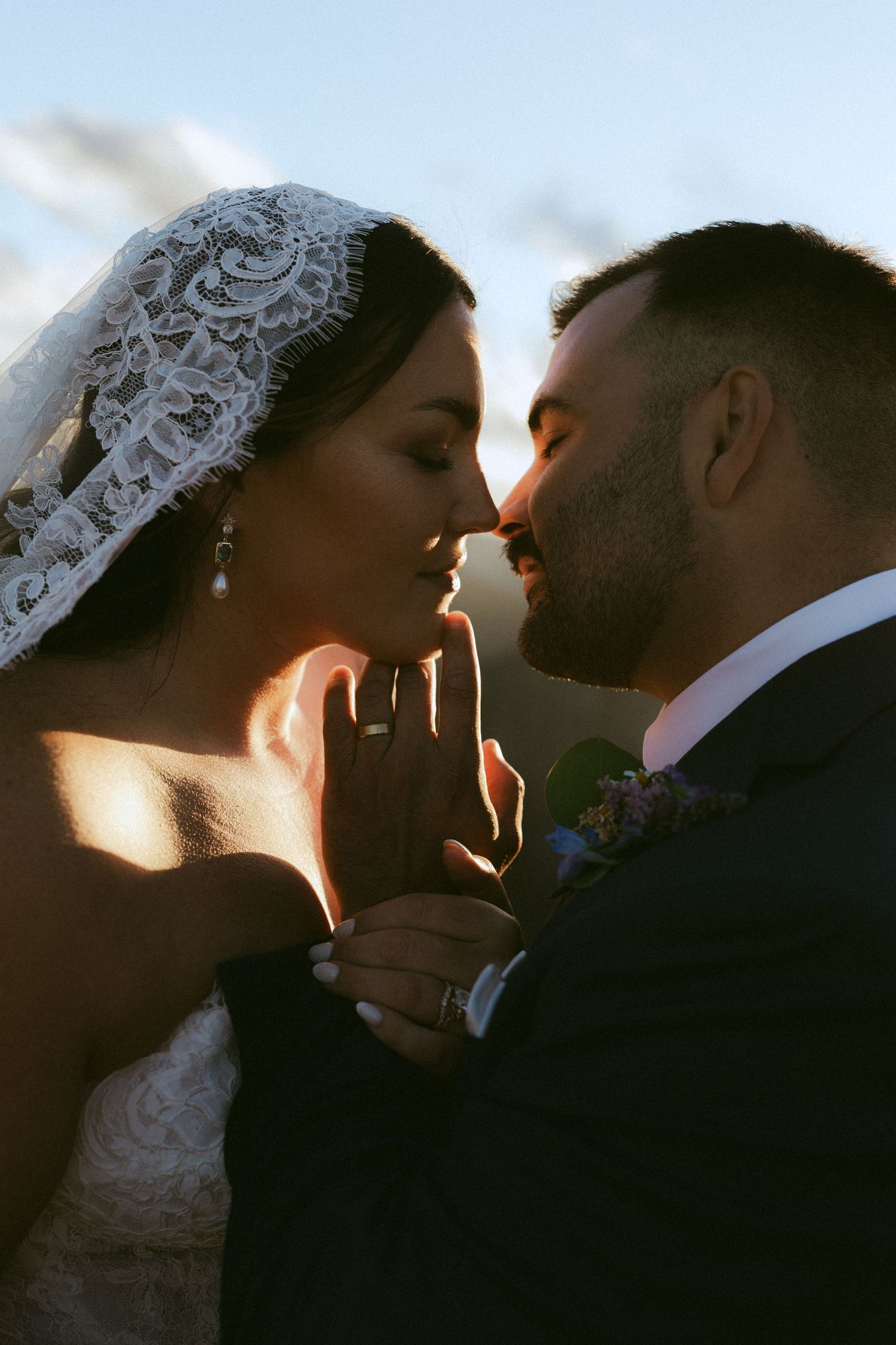 Bride and groom share romantic moment in golden backlit sunlight at wedding.