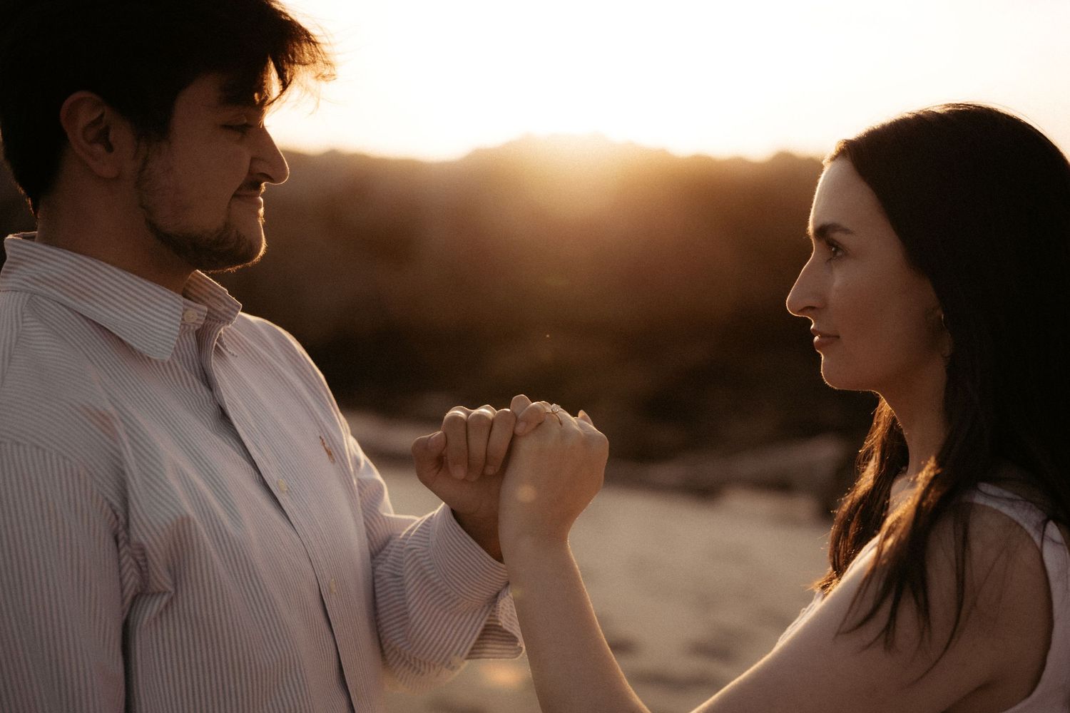 Couple holding hands at golden hour sunset in a romantic outdoor setting.