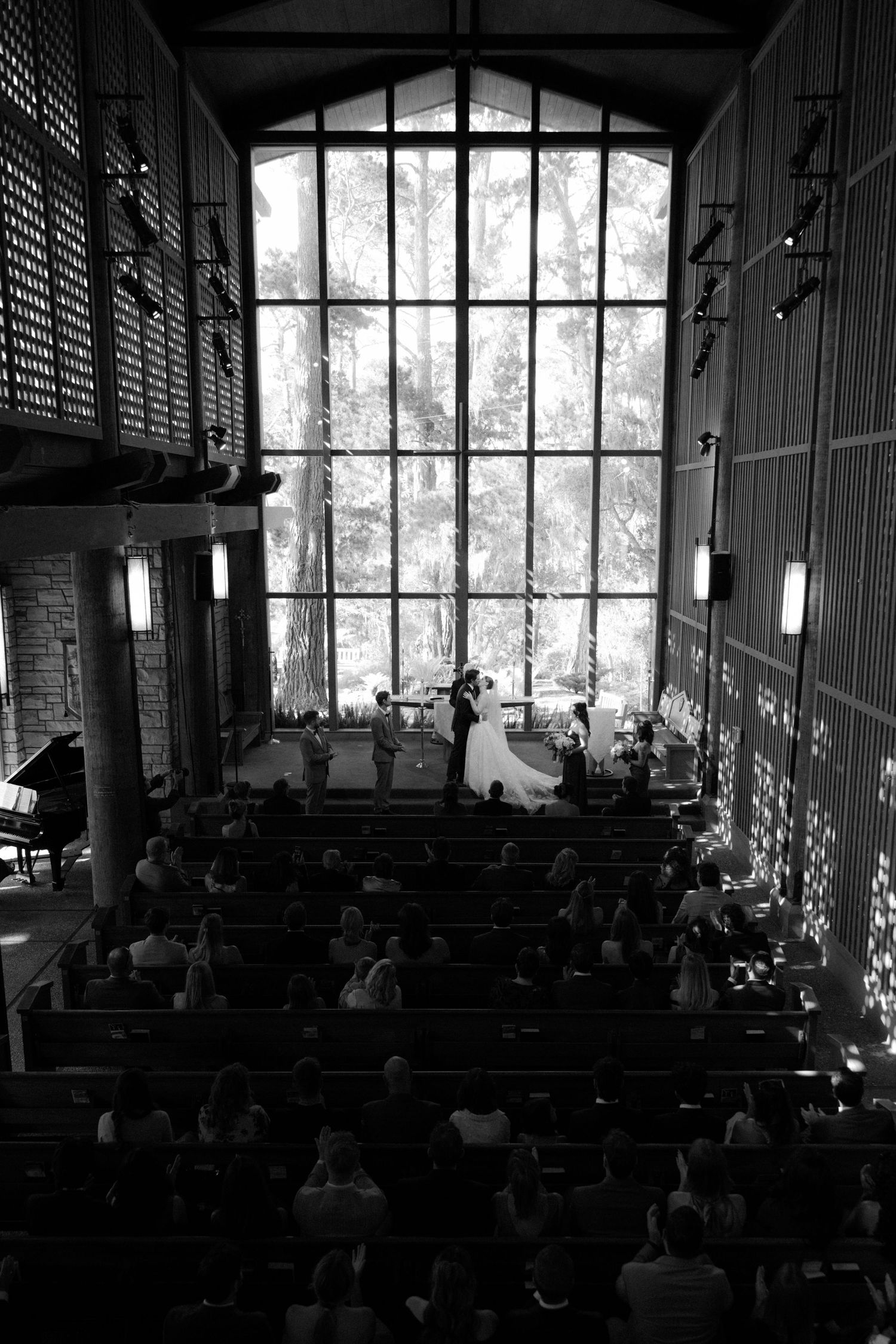 Black and white aerial view of wedding ceremony in modern church with tall windows and seated guests.