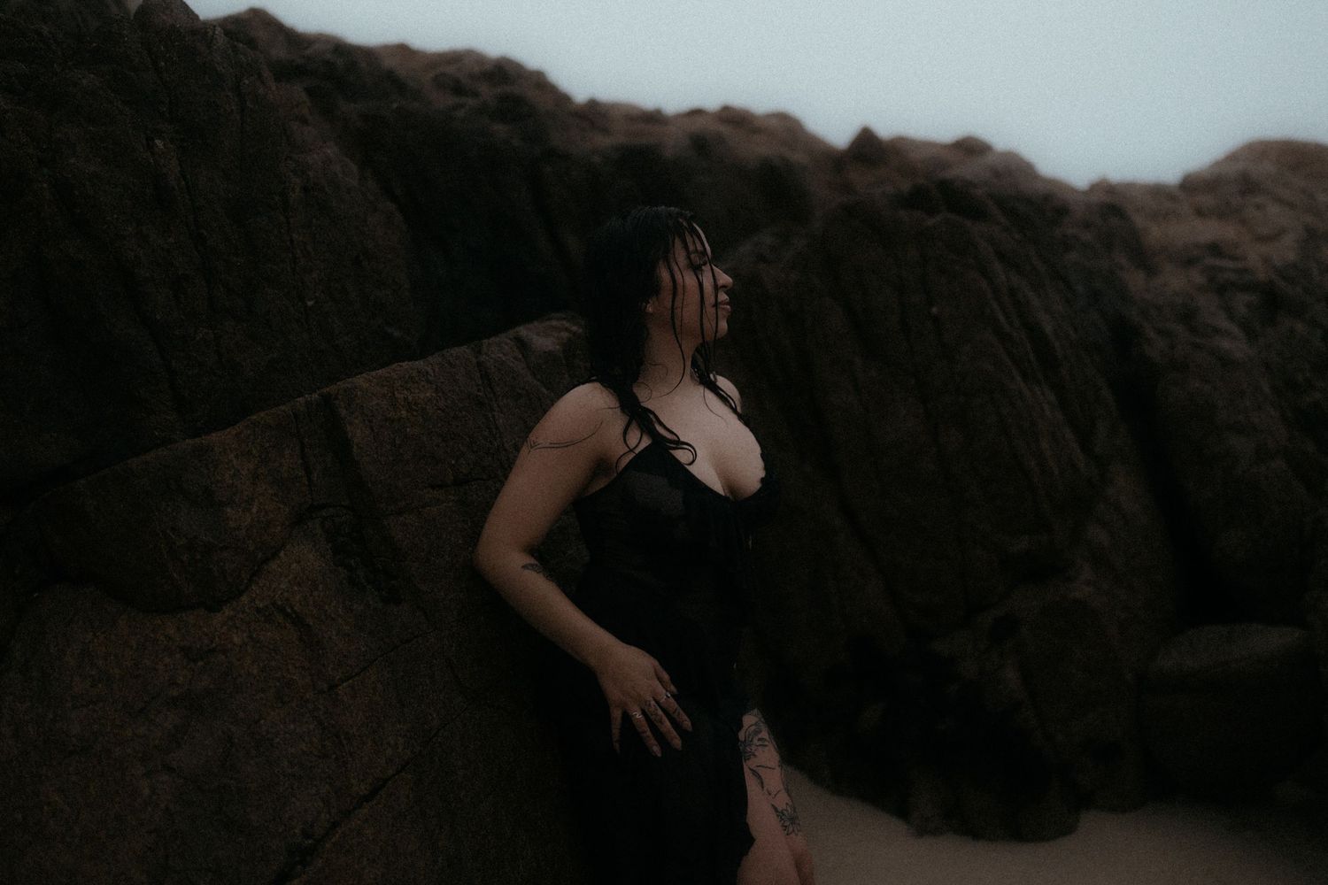 Silhouette figure posing dramatically against a cloudy sky and rocky coastline.