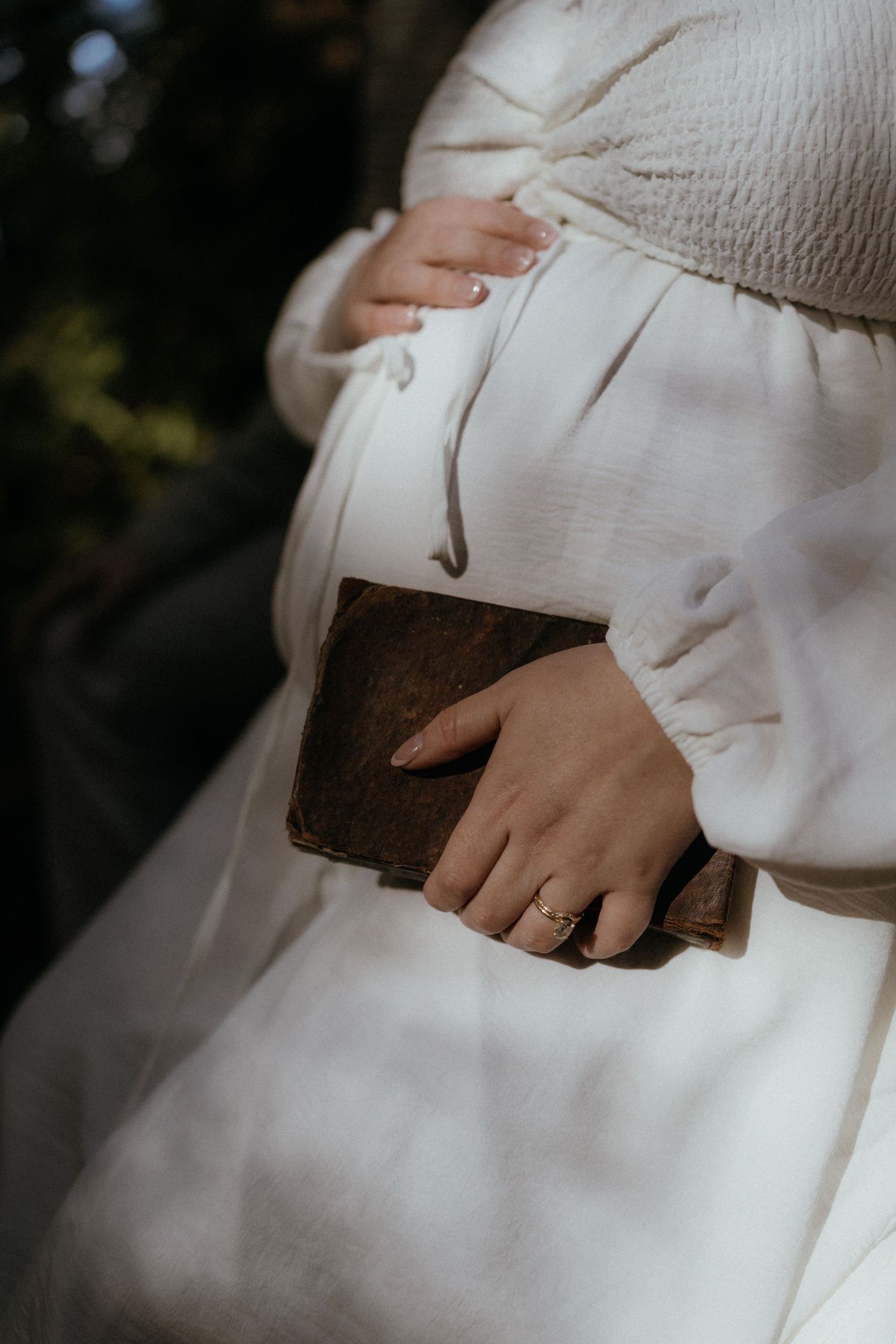 Close-up detail of hands holding a brown leather Bible against a white dress in soft natural light.