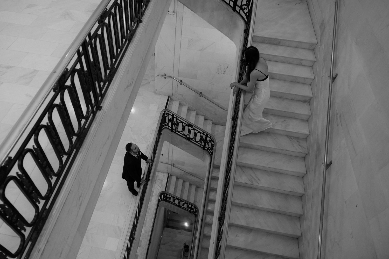 Black and white photograph of a spiral staircase with ornate iron railings viewed from above in an architectural setting.