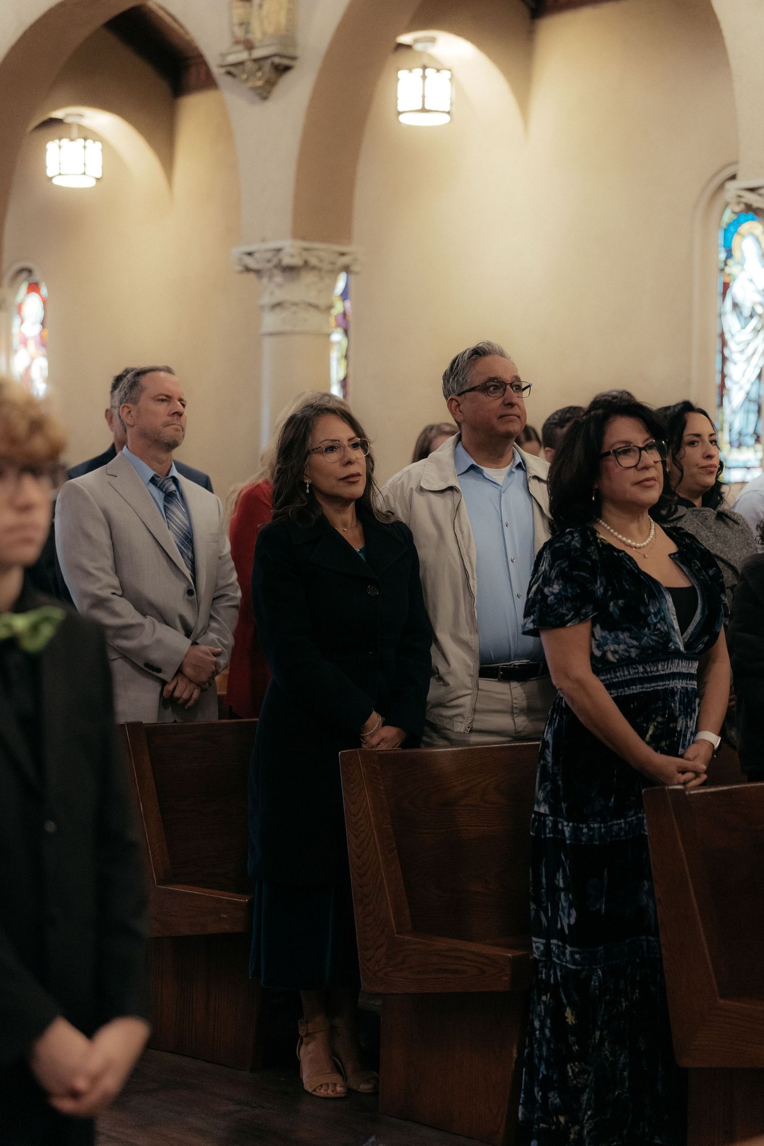Wedding guests stand in wooden church pews during a ceremony.